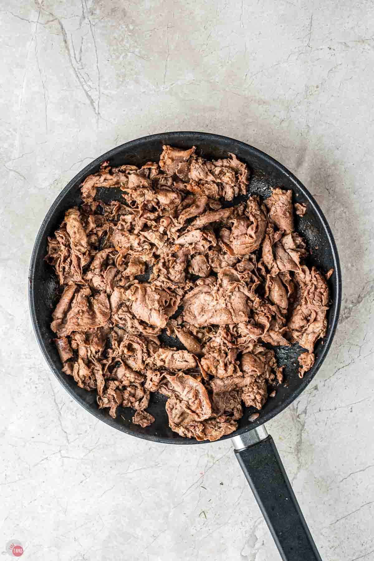 shaved steak cooking in a skillet