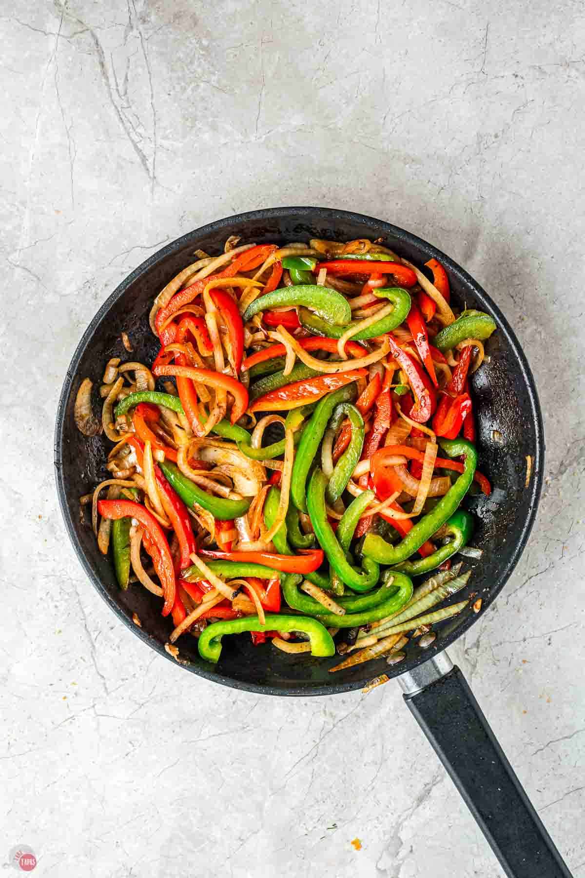 sliced bell peppers and onions cooking in a skillet