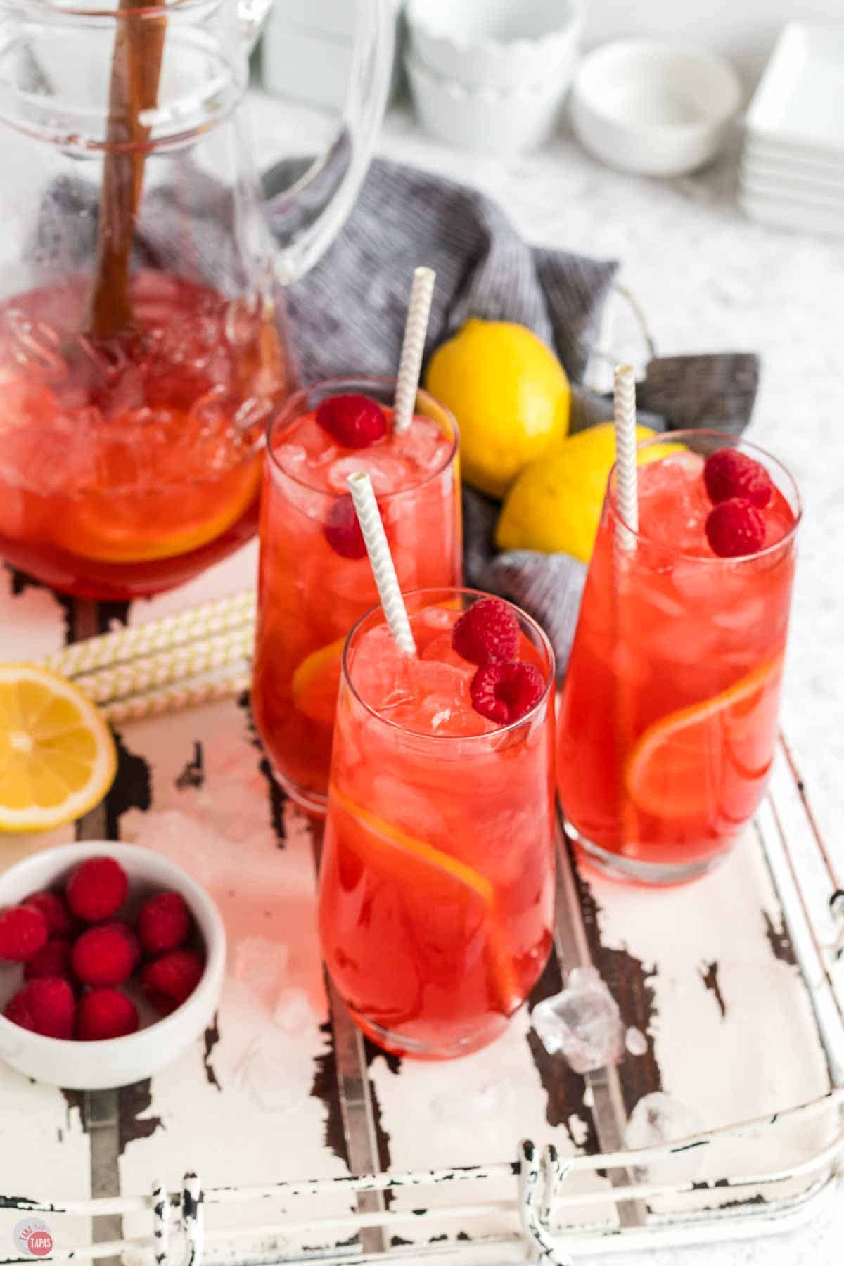 three glasses of raspberry iced tea with lemons on a white tray