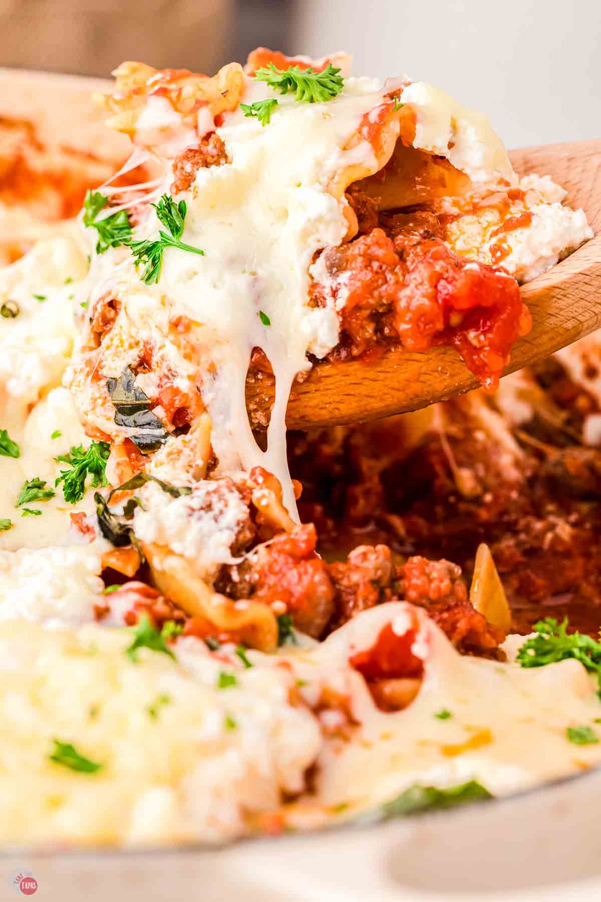 close up of wood spoon scooping lasagna out of a pan