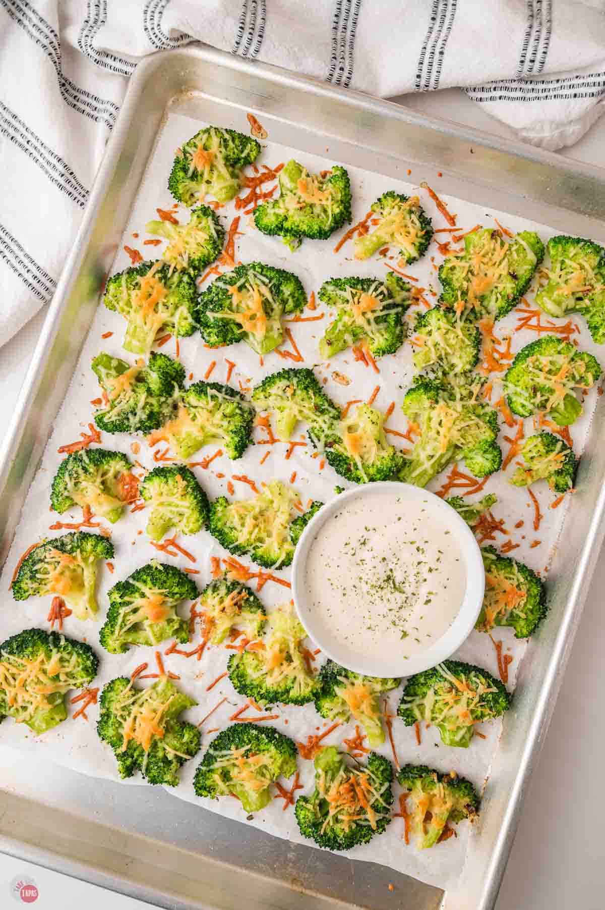 baking dish of baked broccoli that is smashed and topped with cheese