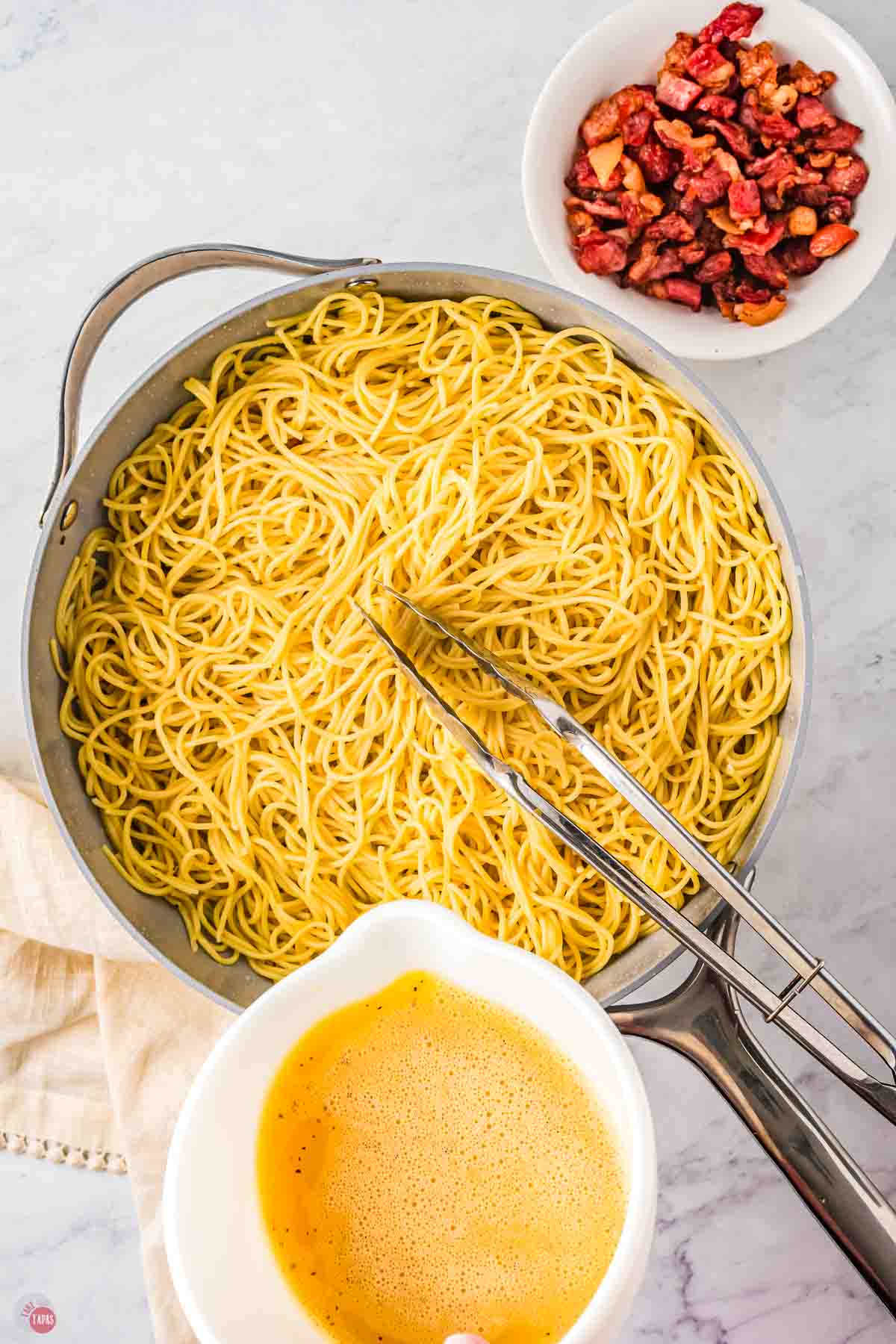 skillet of cooked spaghetti with beaten eggs being poured in