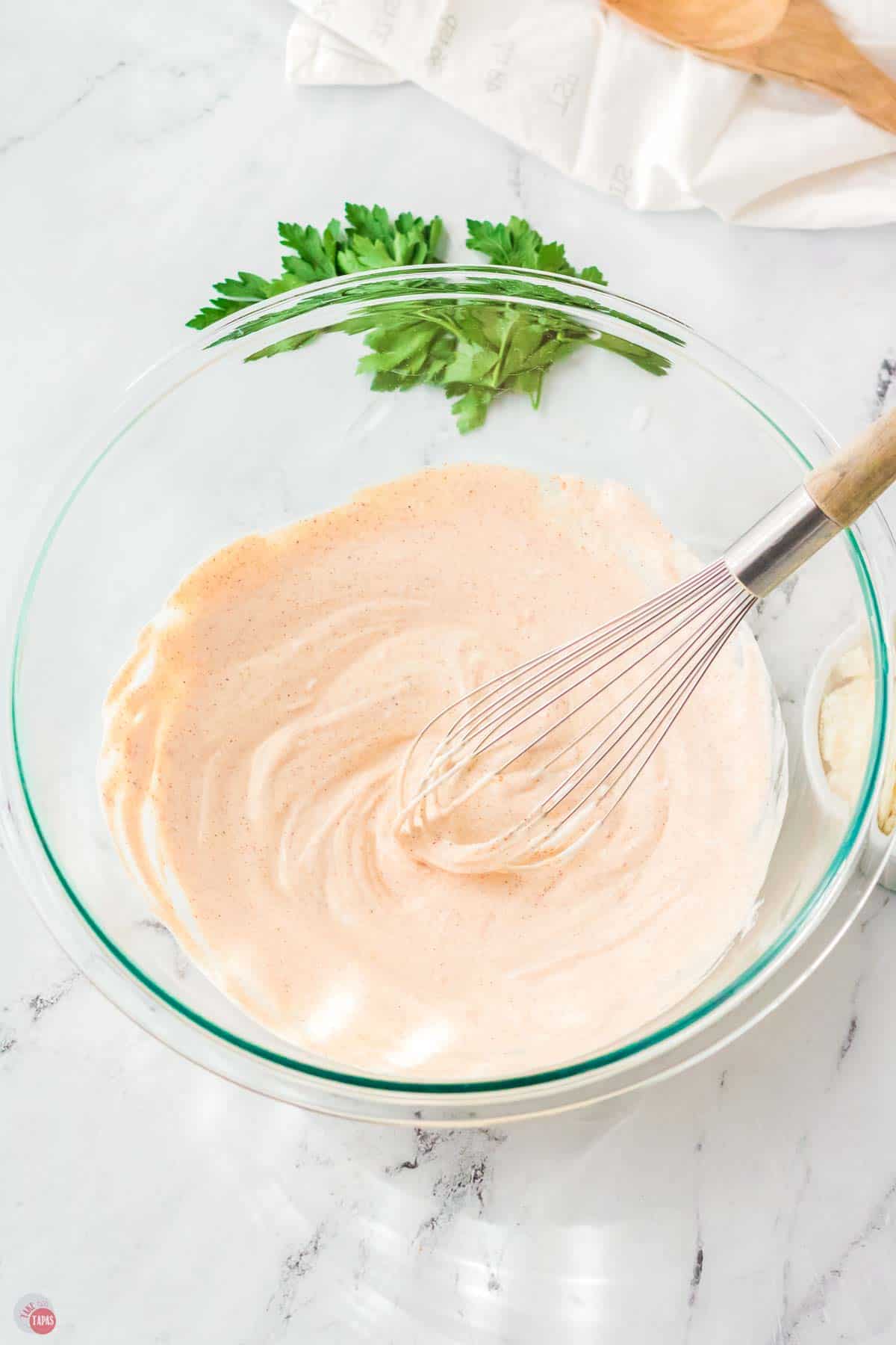 bowl of creamy dressing with a whisk stirring it
