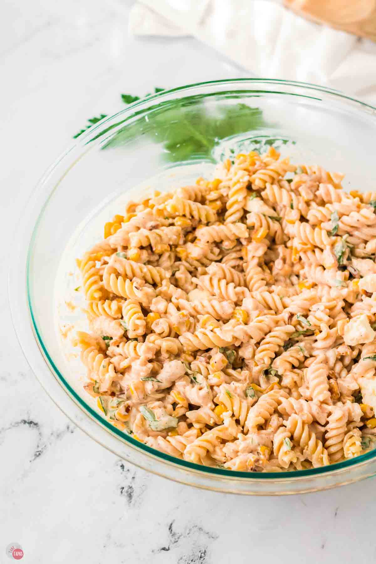 close up of pasta salad in a clear bowl with cilantro behind it