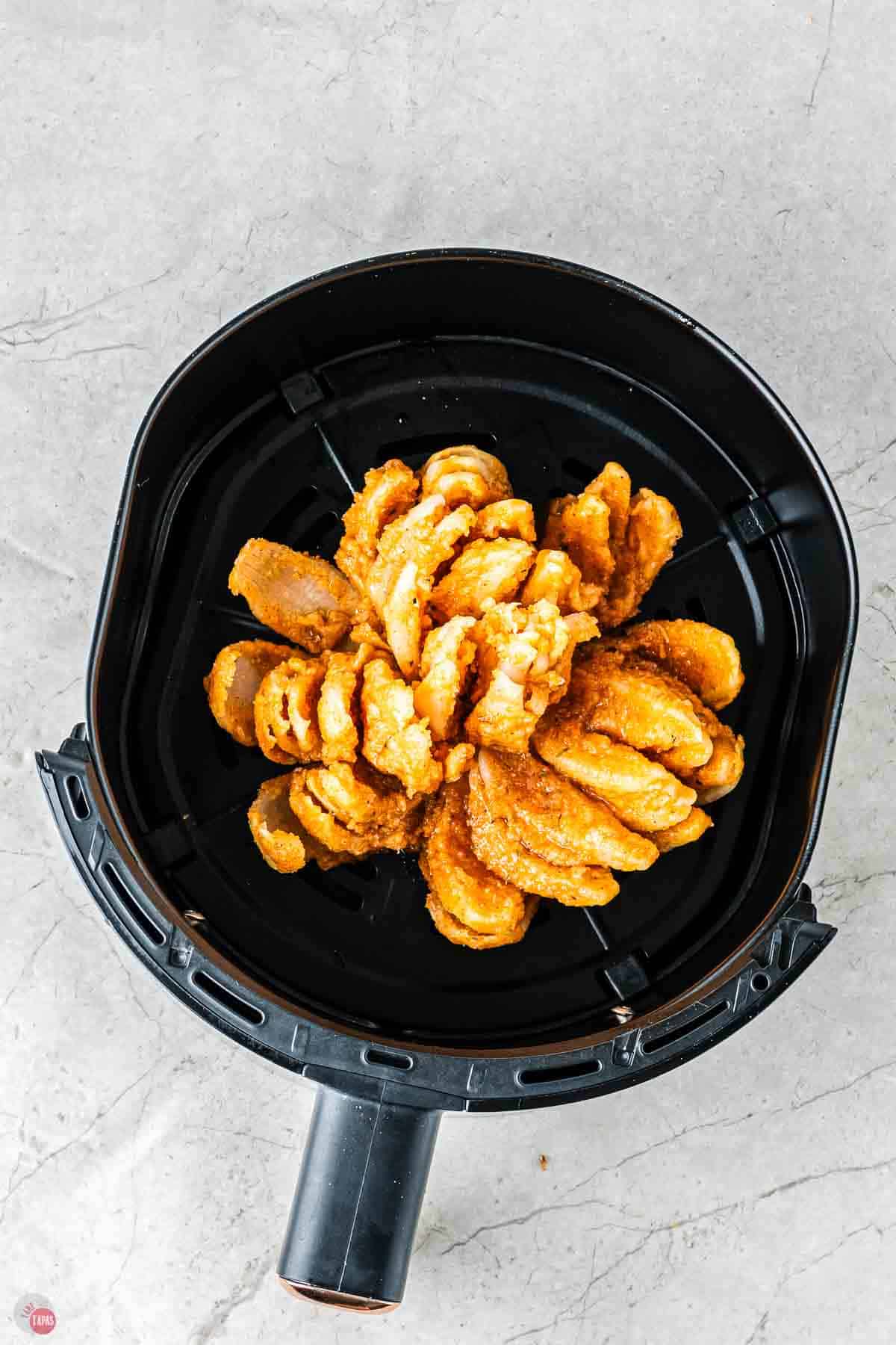 a coated onion flower in an air fryer basket