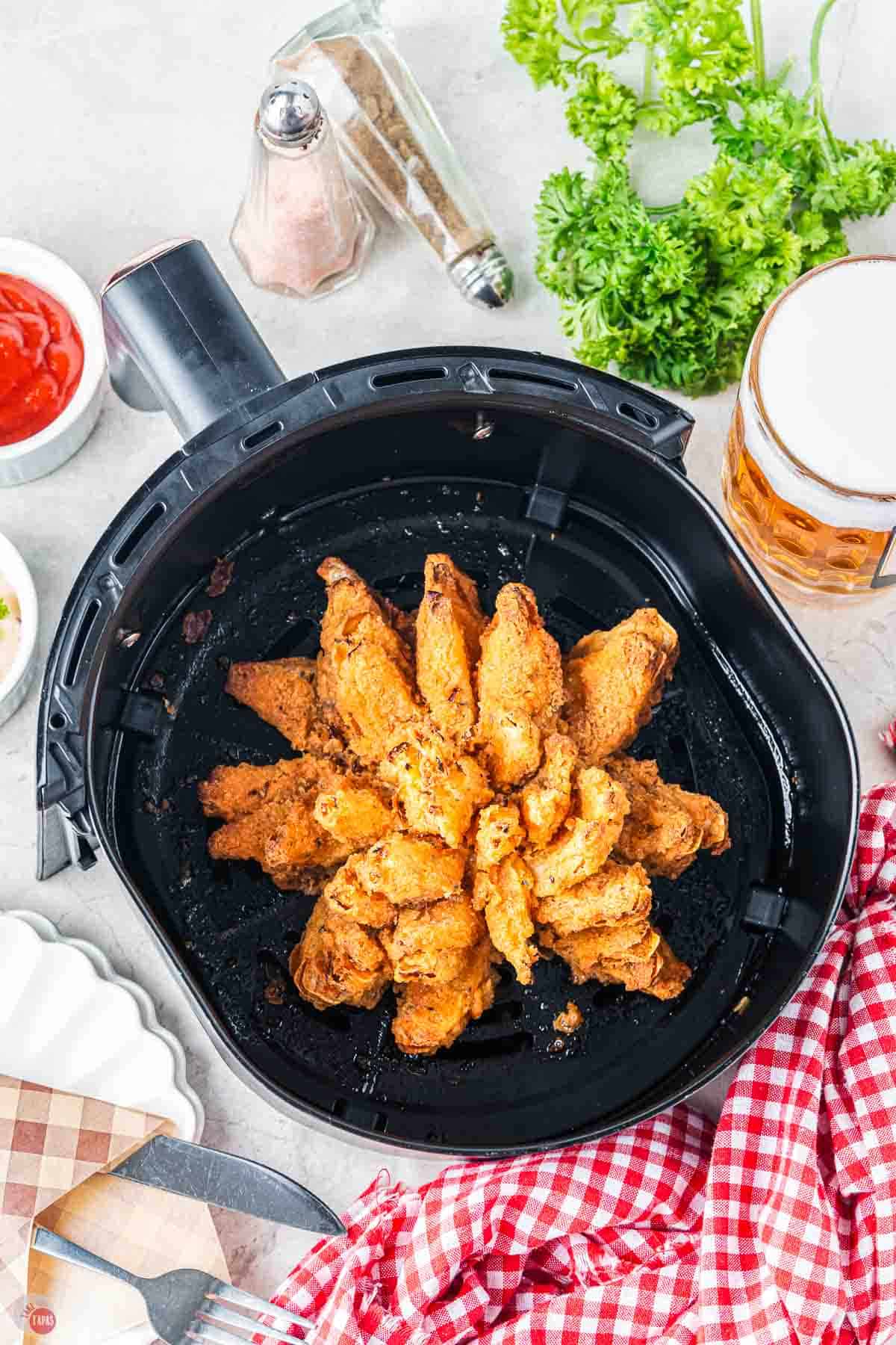 air fried blooming onion in a basket with dipping sauces and a napkin