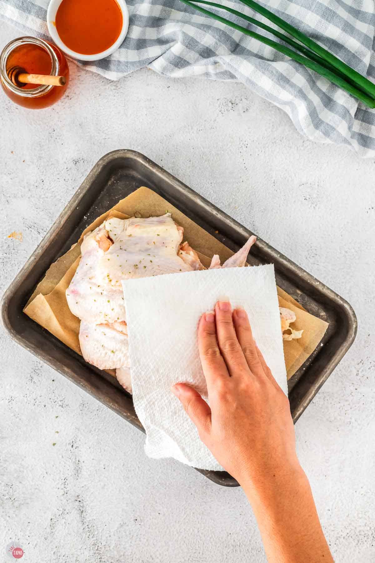 wings on a baking sheet being patted with a paper towel
