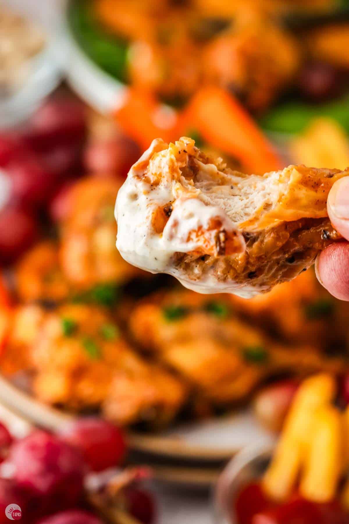 close up of hand holding a chicken wing dipped in ranch dressing with a bite missing