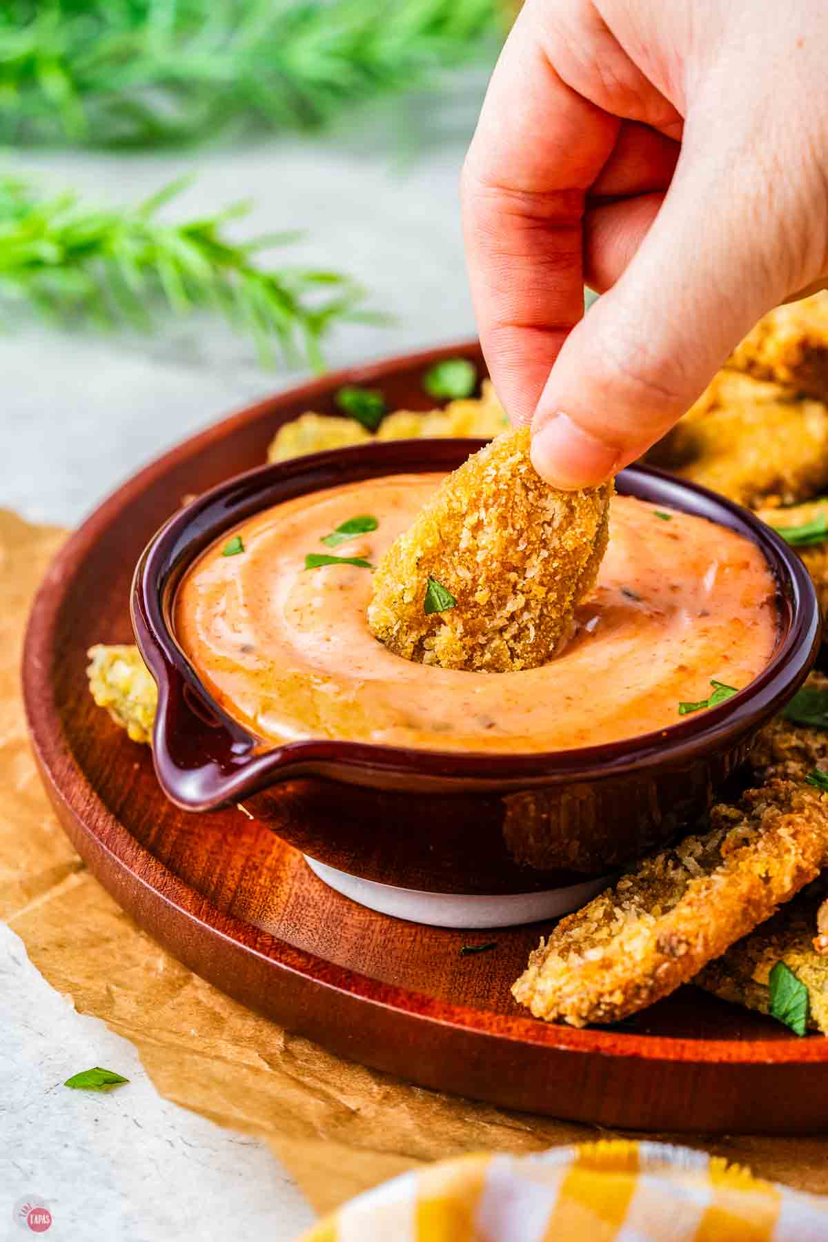 hand dipping a fried pickle in a small bowl of dip