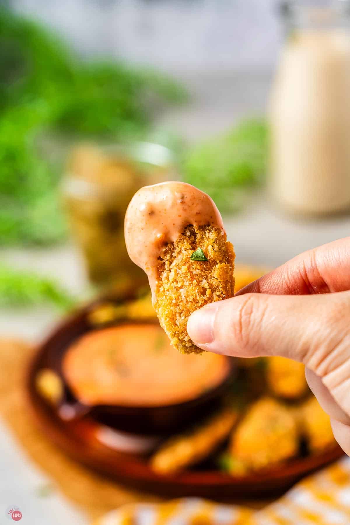 hand holding a fried pickle with dip on the top of it