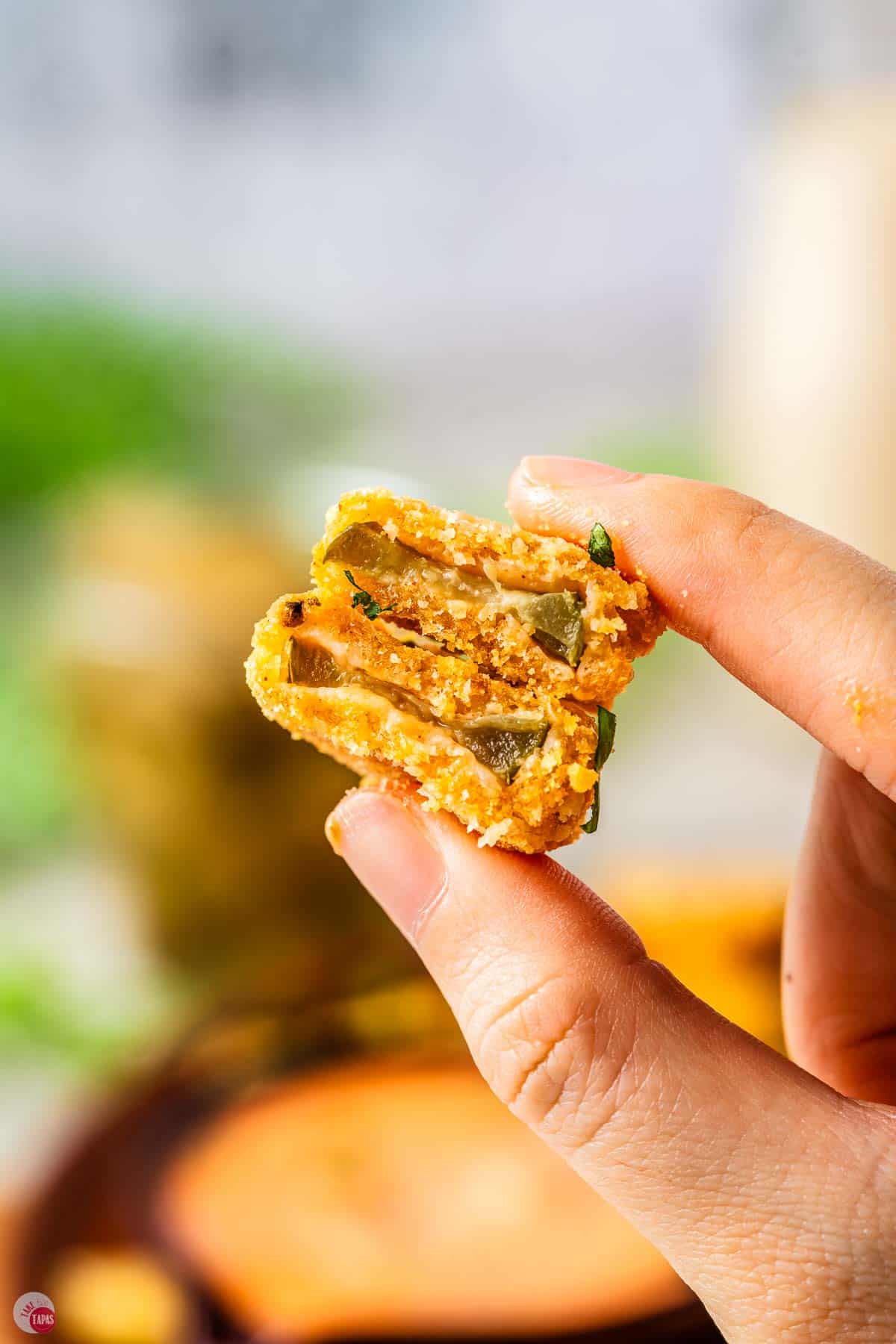 hand holding two fried pickles with bites taken out of them