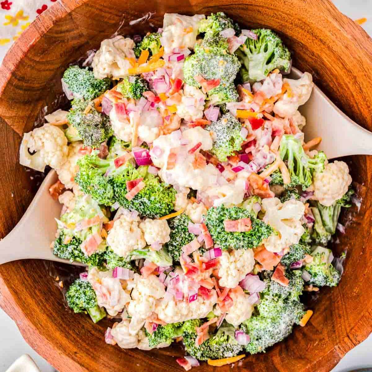 wood bowl filled with broccoli salad with two wood spoons