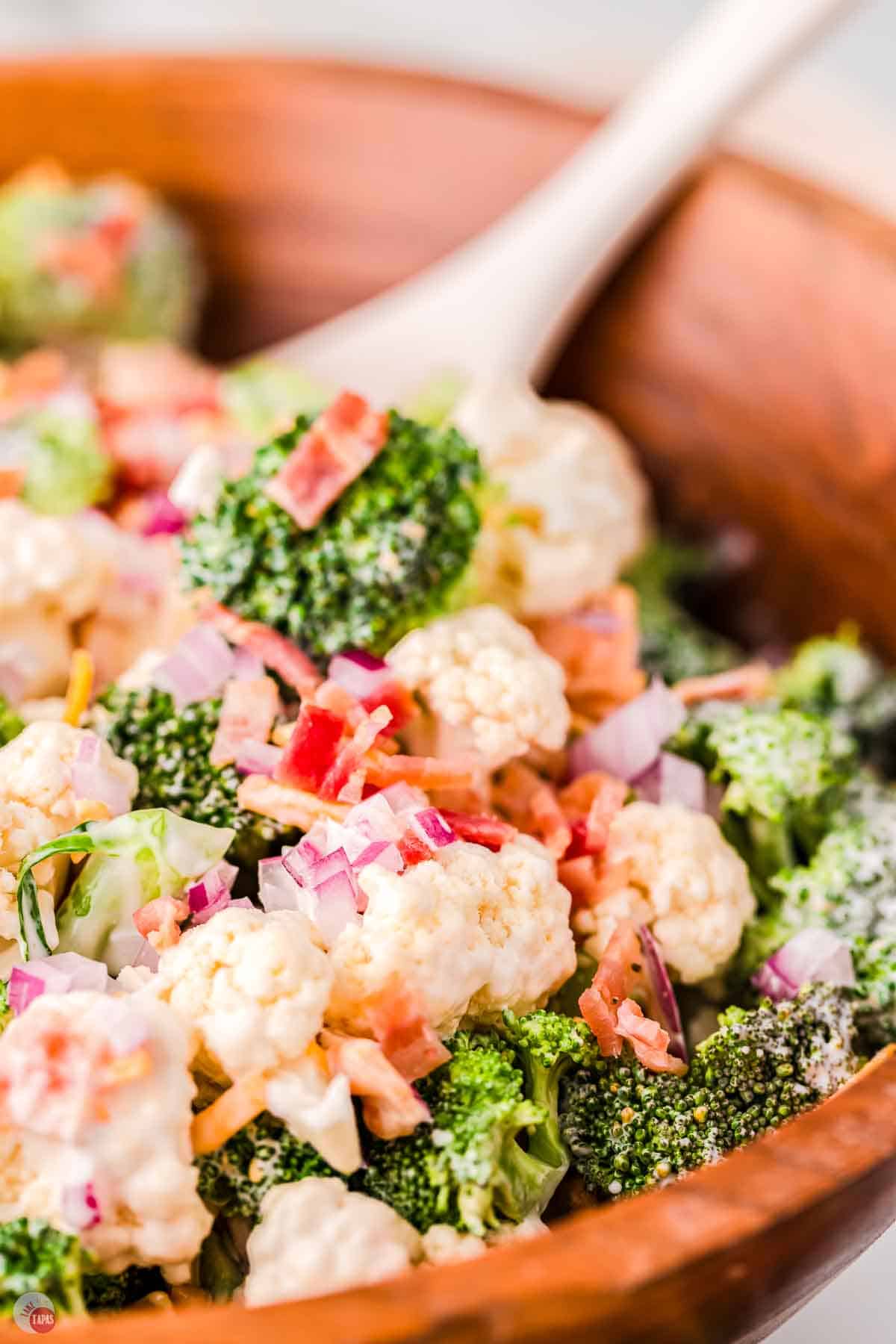 closeup of broccoli and cauliflower florets tossed in dressing and topped with bacon and cheese