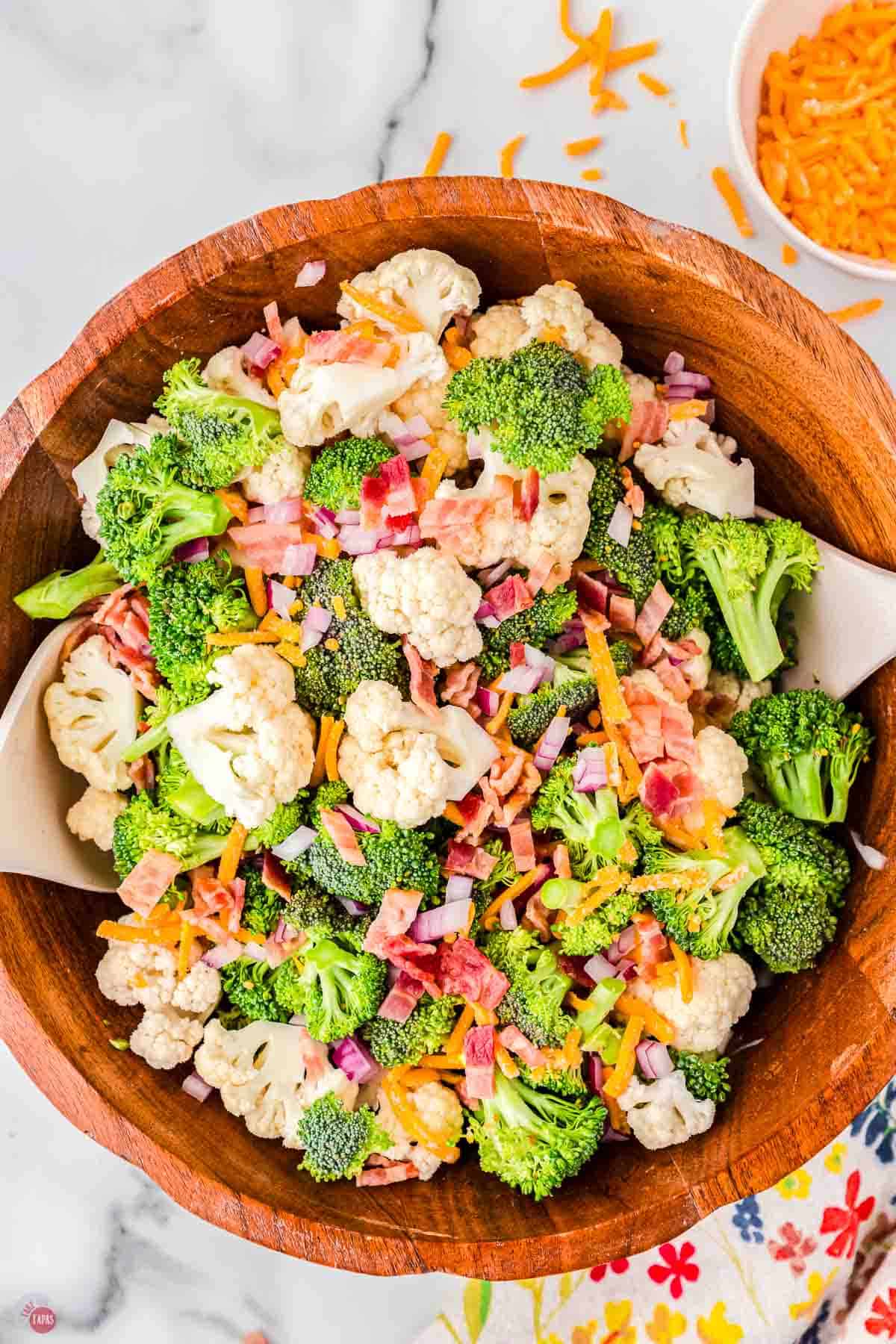 wood bowl with two spoons stirring up raw vegetables