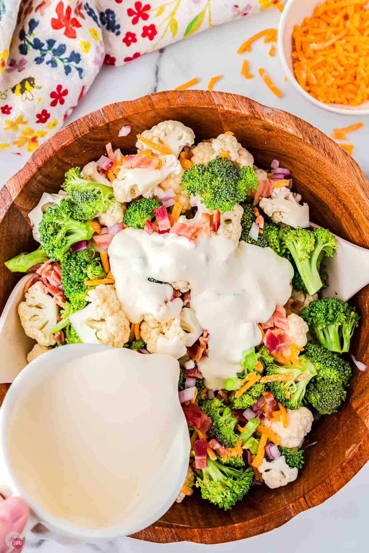 raw vegetables in a bowl with creamy dressing being poured over them