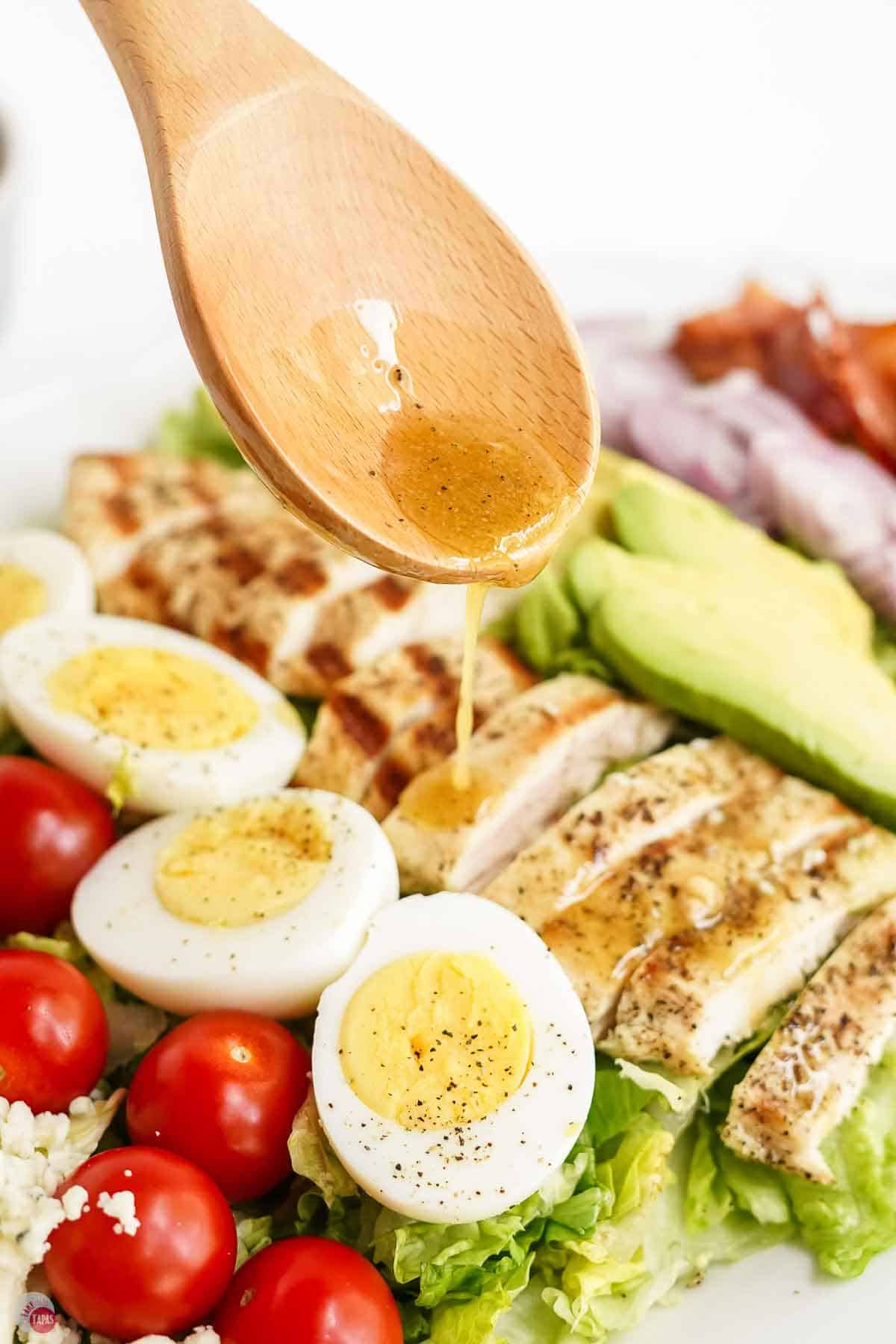 wood spoon pouring salad dressing over grilled chicken and lettuce