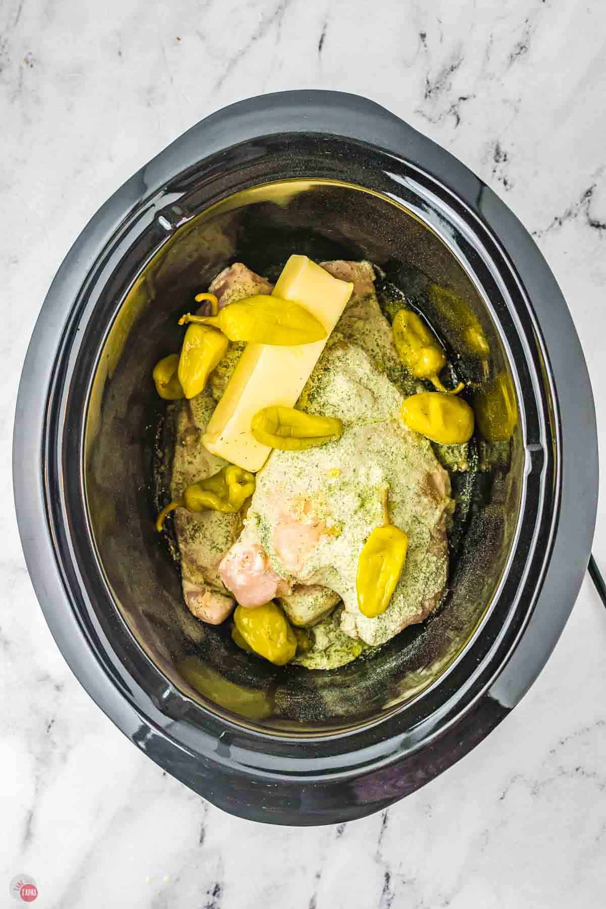 chicken in a crockpot topped with butter and peppers