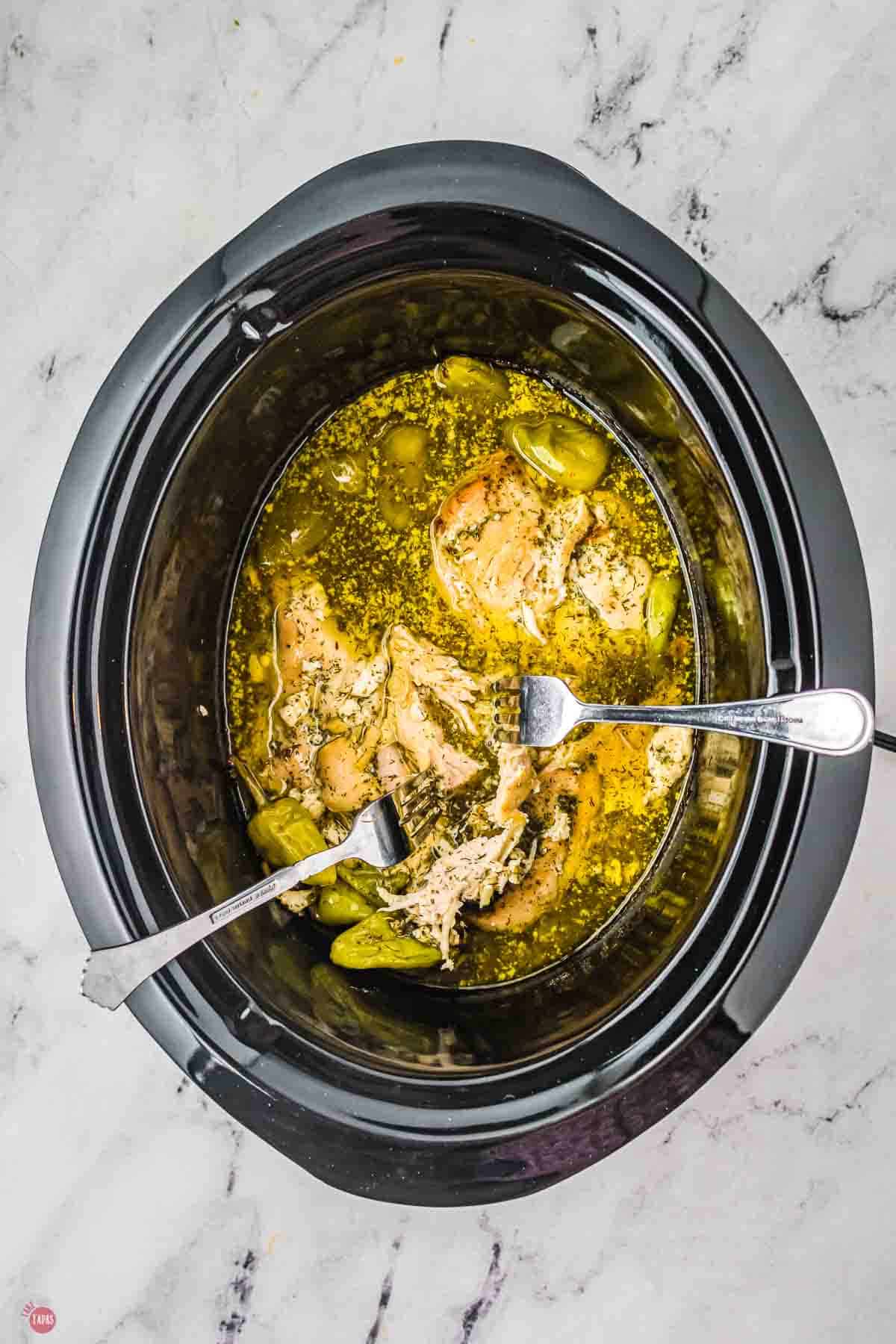 two forks shredding chicken meat in a crockpot