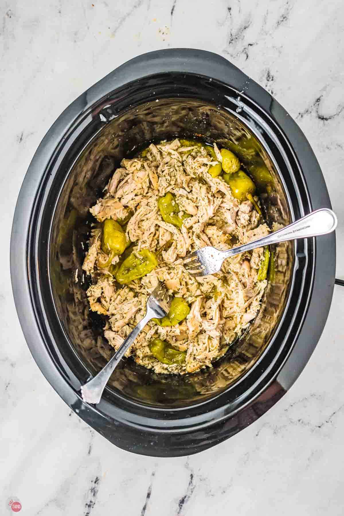 black slow cooker with shredded chicken and two forks