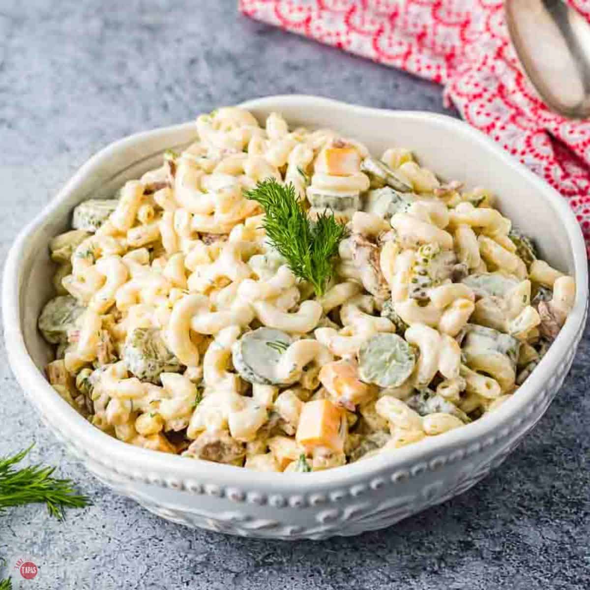 white bowl filled with tangy pasta salad next to a white and red napkin
