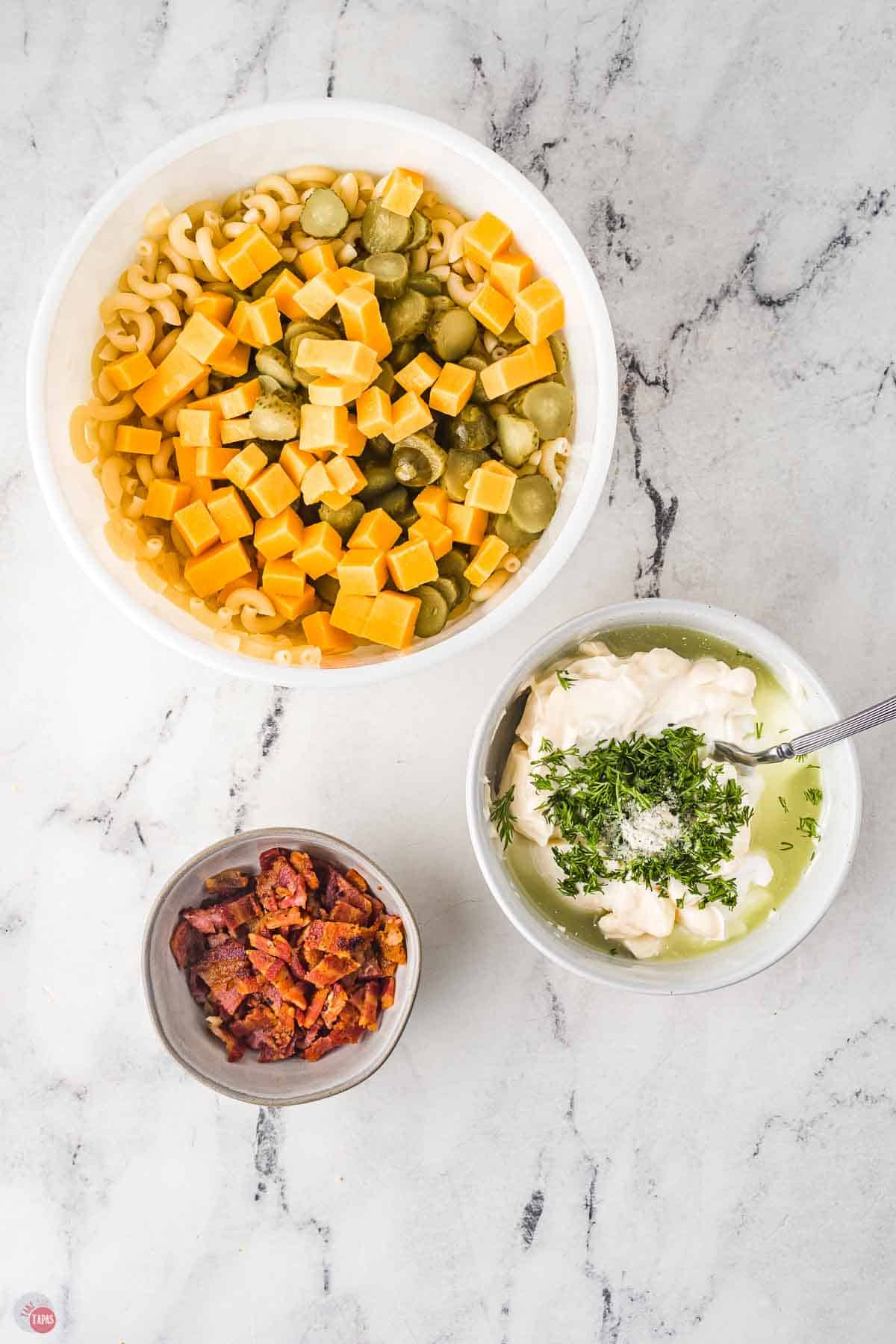 two bowls, one with cooked pasta noodles and the other with a creamy dressing being mixed