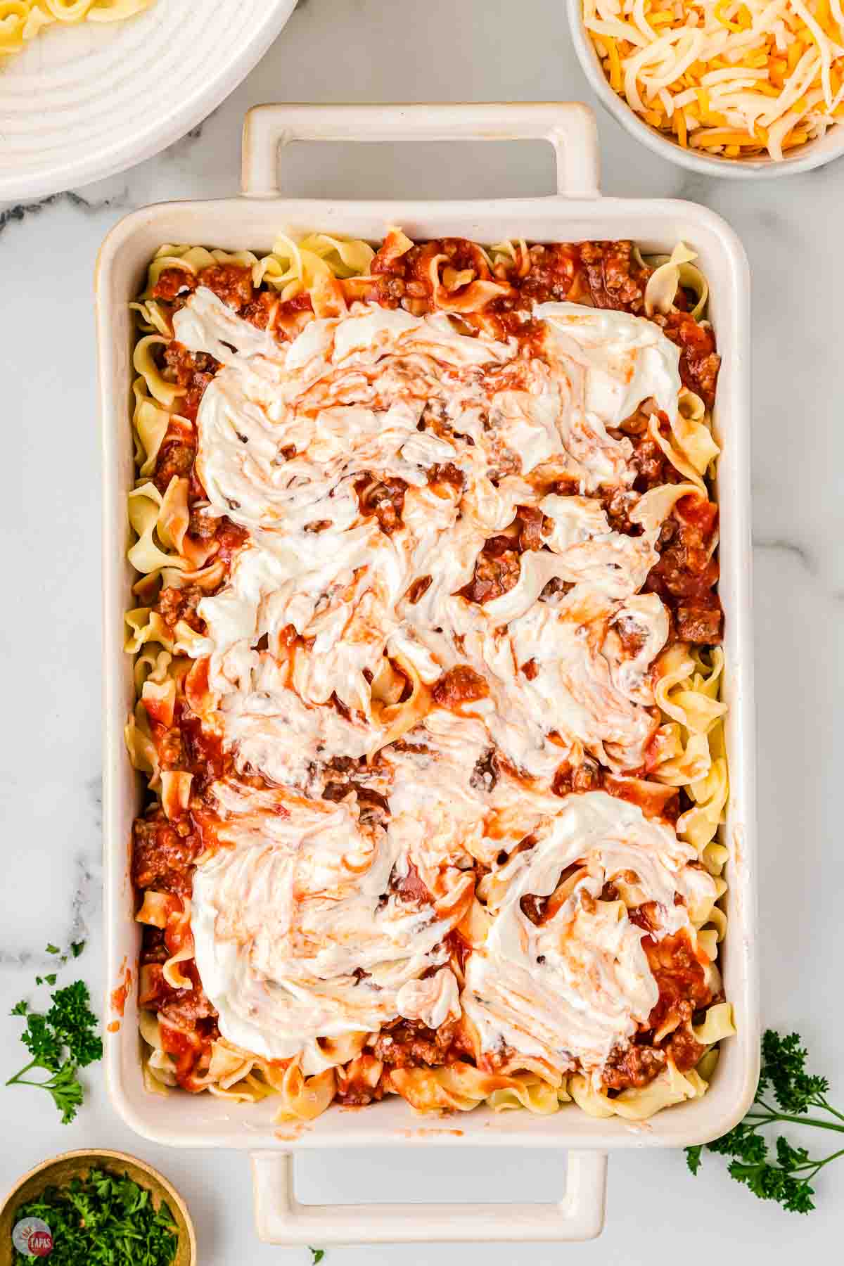 noodles and sauce in a casserole dish topped with swirls of cheese sauce
