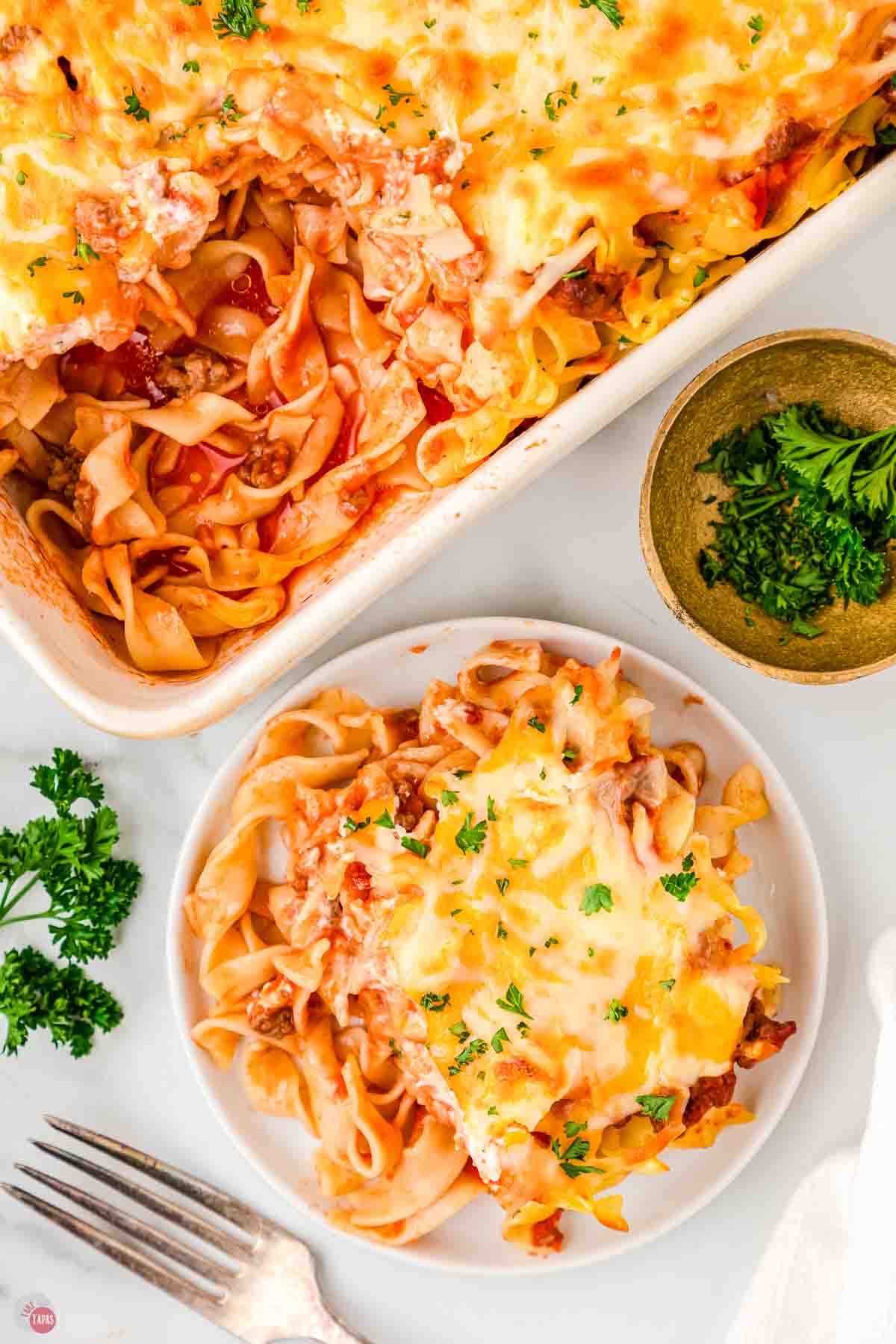 plate of casserole next to a dish with chopped parsley