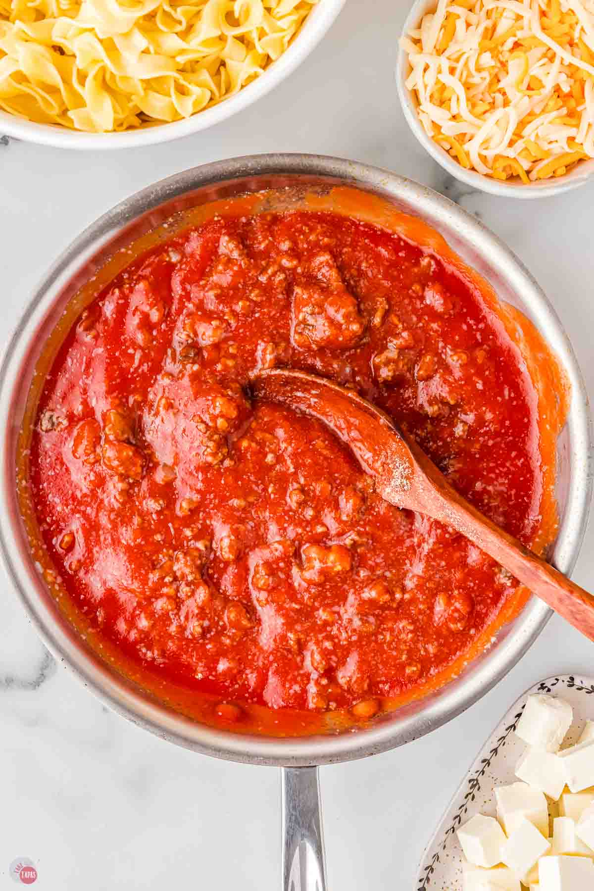 skillet with meat sauce being stirred by a wood spoon