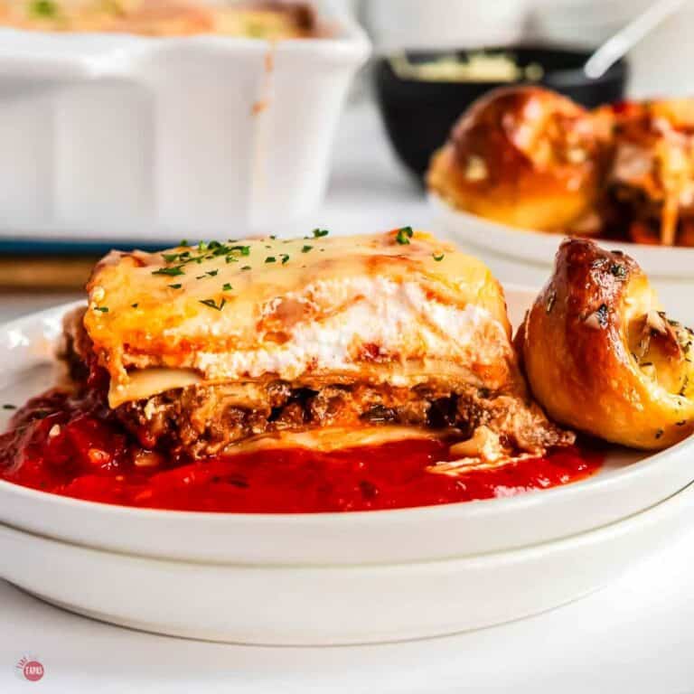 white plate with slice of lasagna and a garlic knot