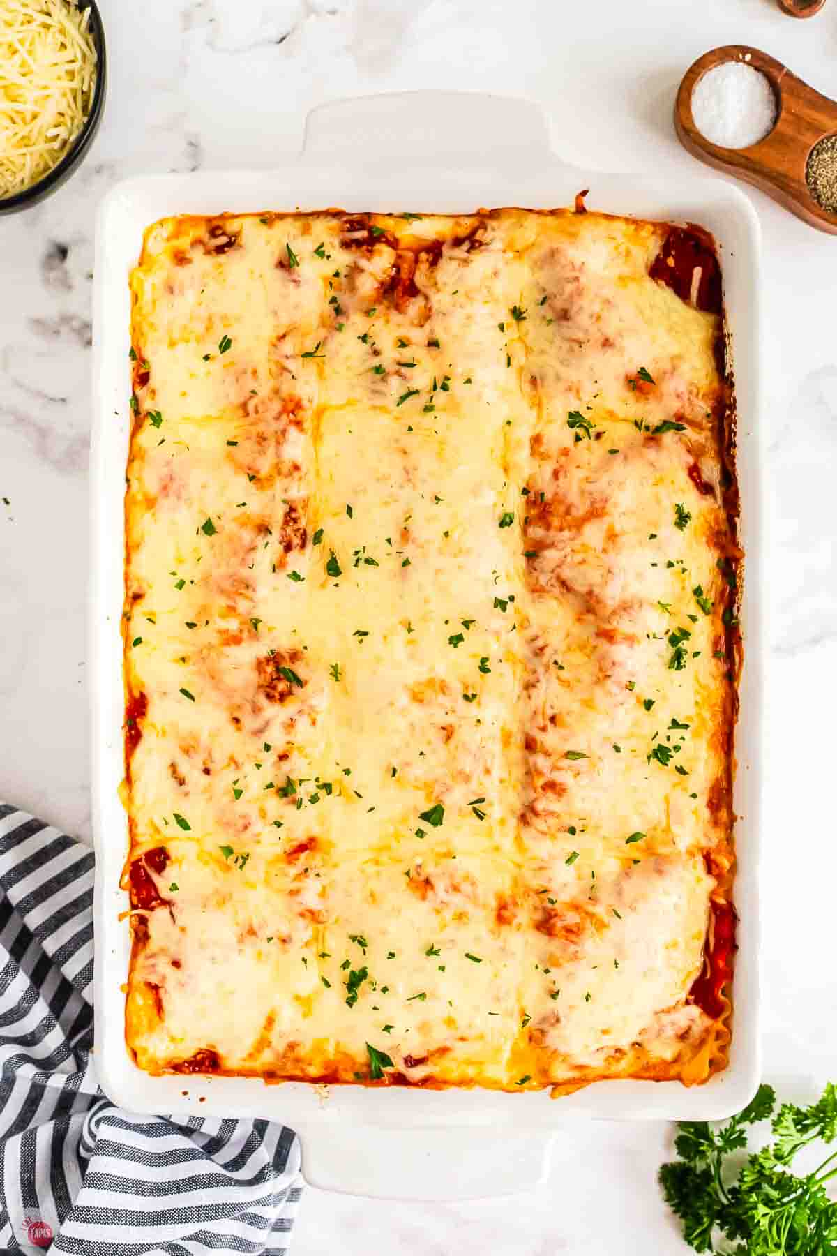 baked homemade lasagna in a white dish with a striped napin under it