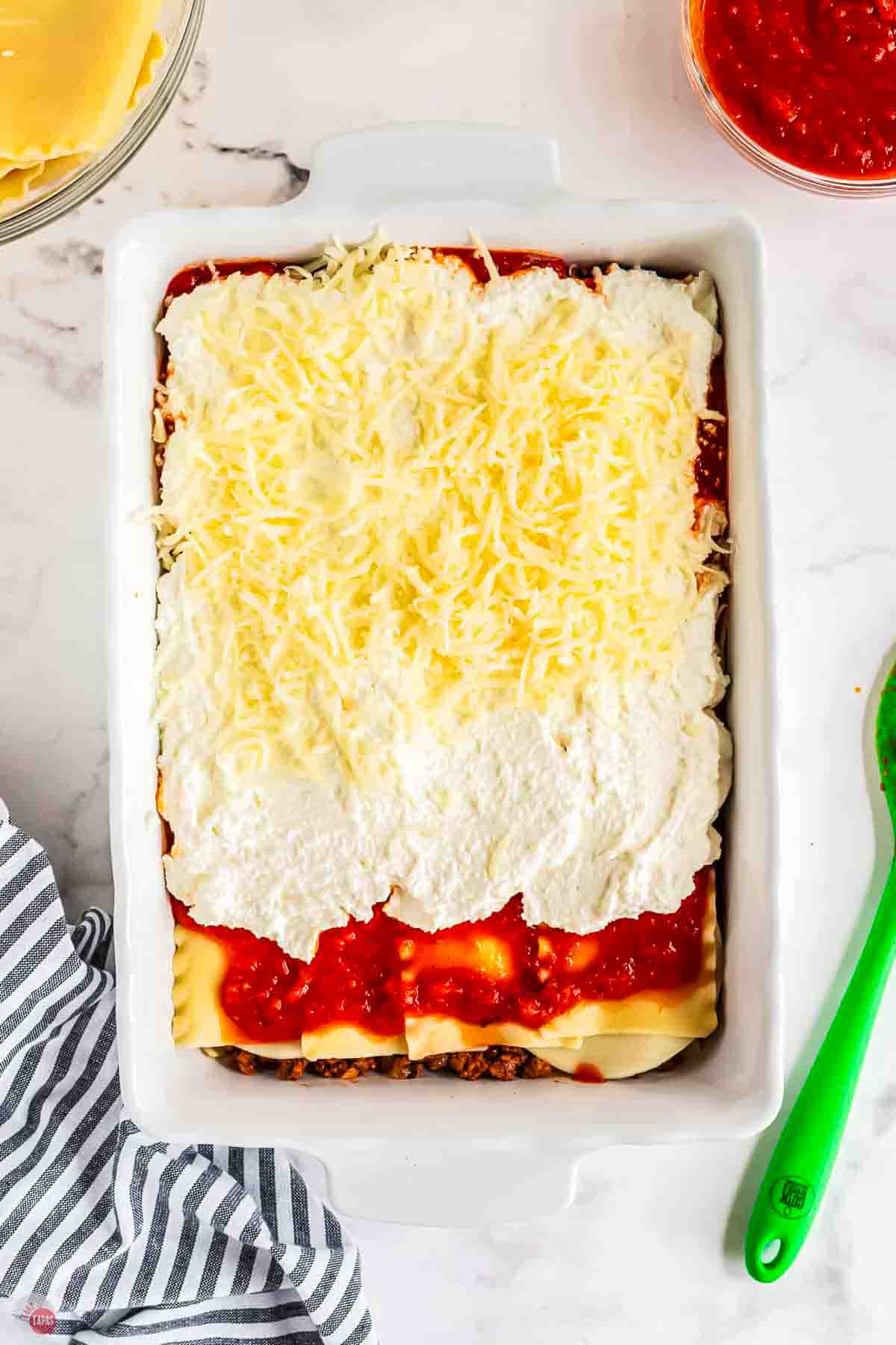 lasagna being layered in a white casserole dish