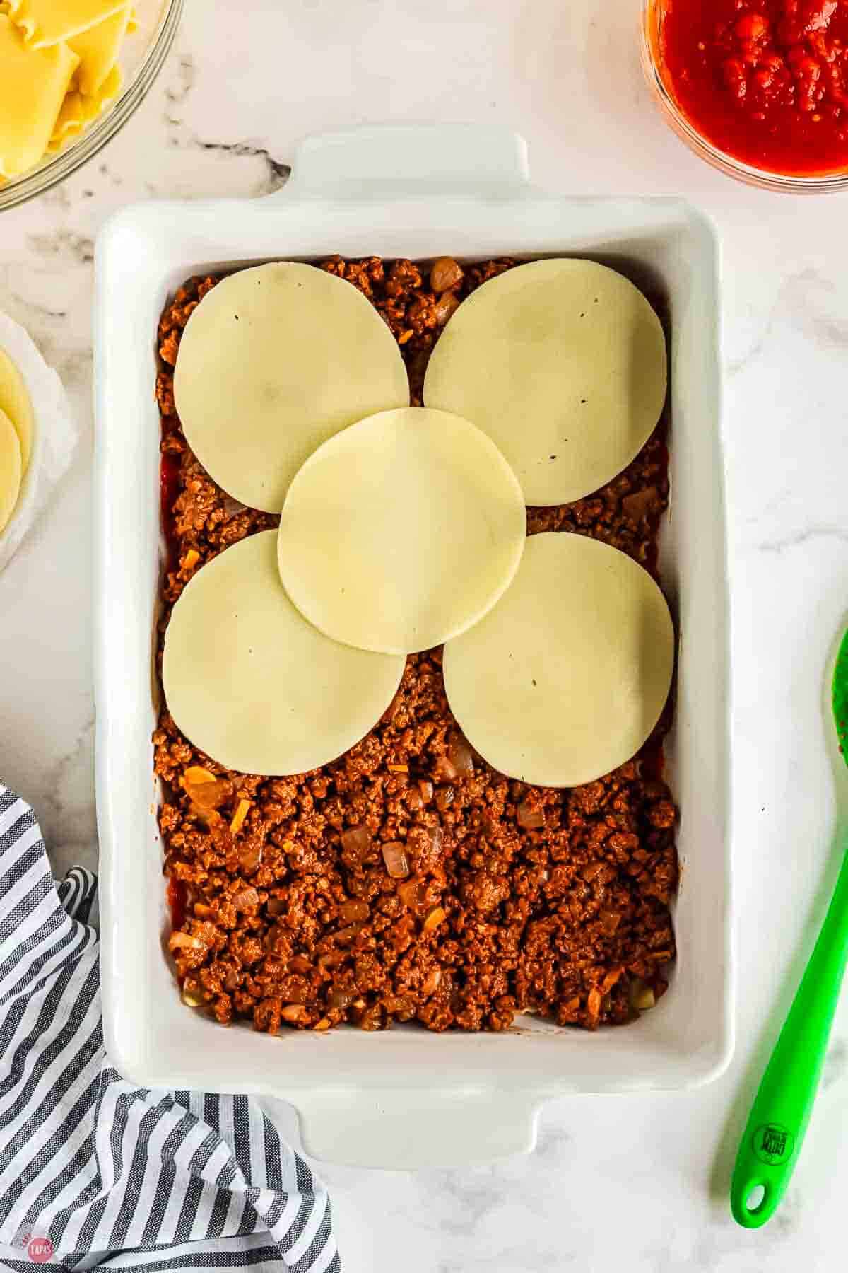 casserole dish with meat layer and slices of provolone cheese on top