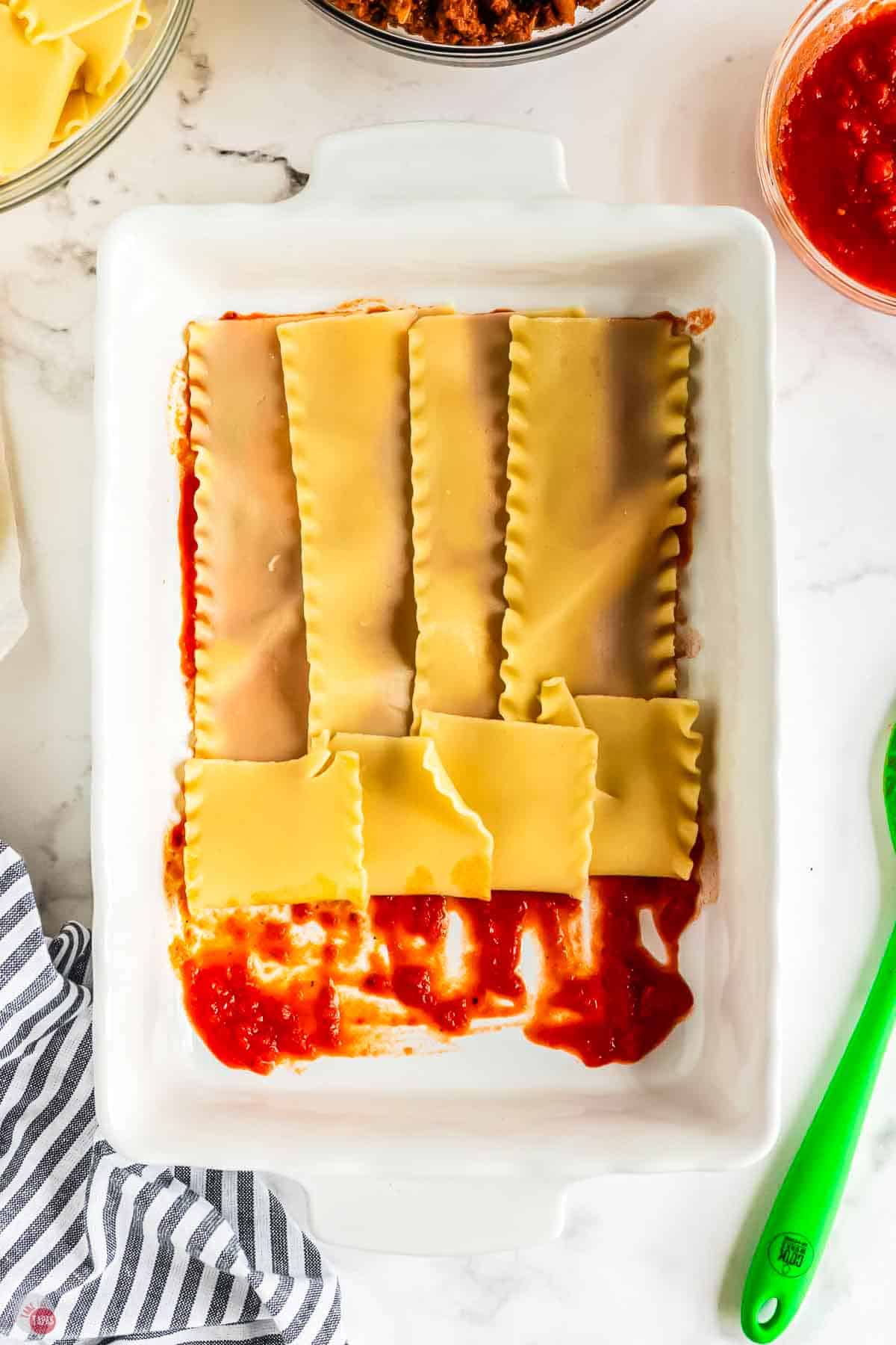 lasagna noodles over sauce in a white baking dish