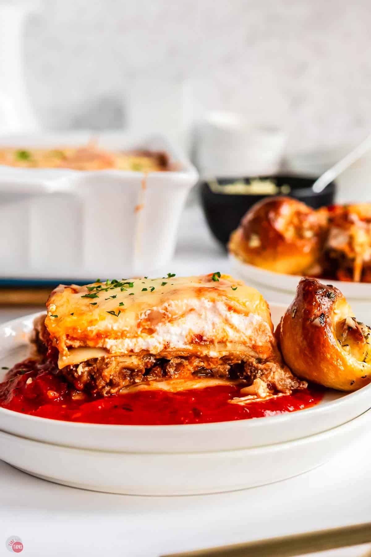 white plate with slice of lasagna and a garlic knot