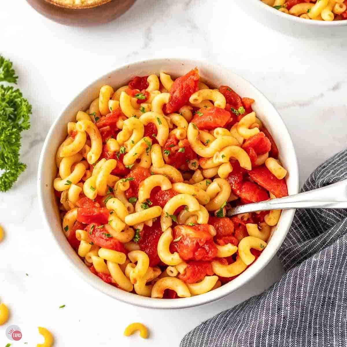 overhead picture of white bowl with a spoon and a blue napkin filled with pasta and sauce