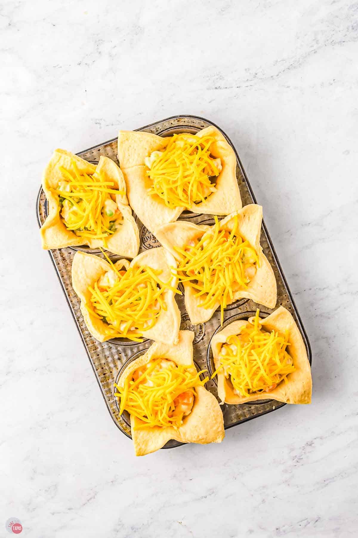 muffin pan with dough squares filled with chicken and topped with shredded cheese