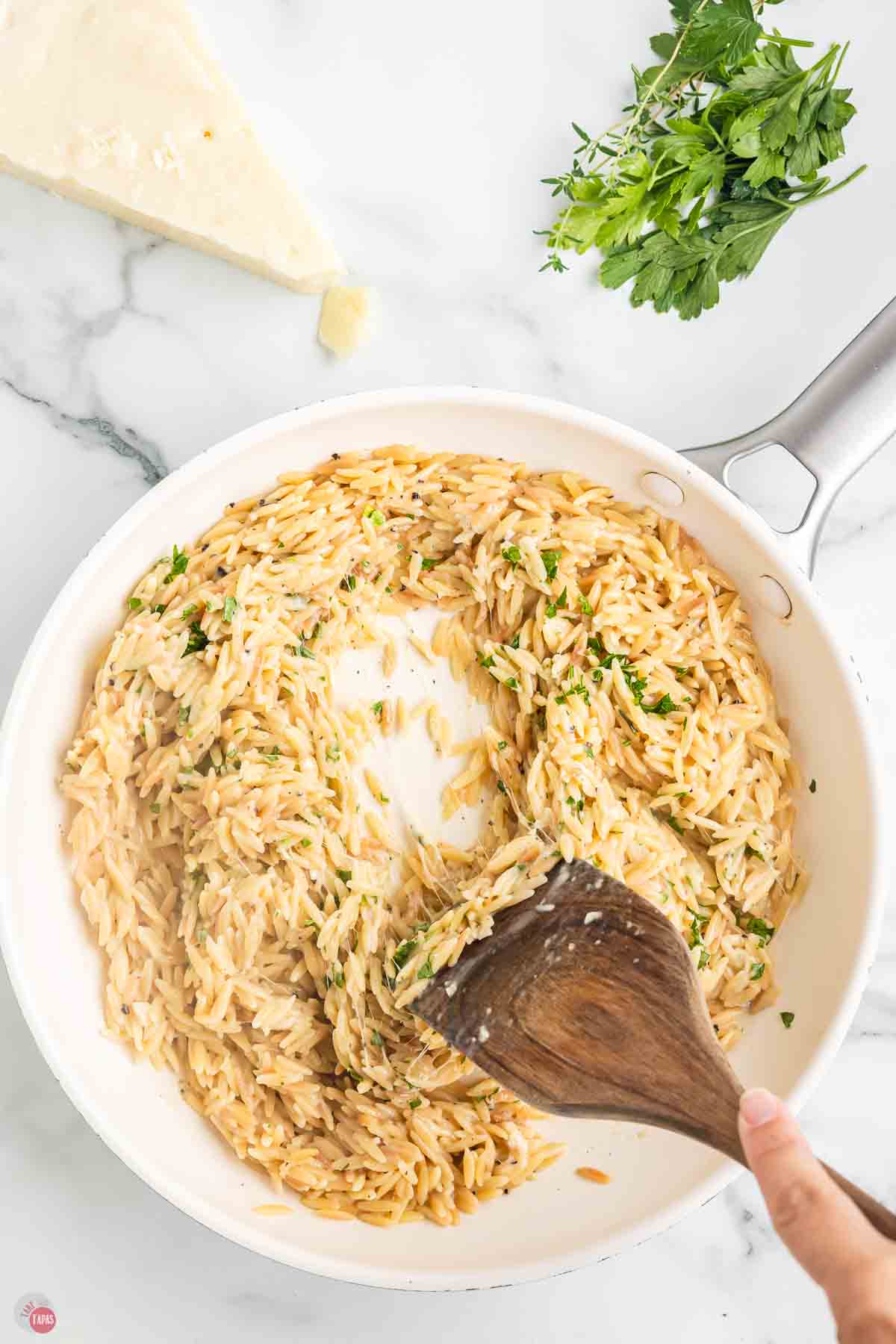 wood spoon stirring pasta and parsley in a white skillet