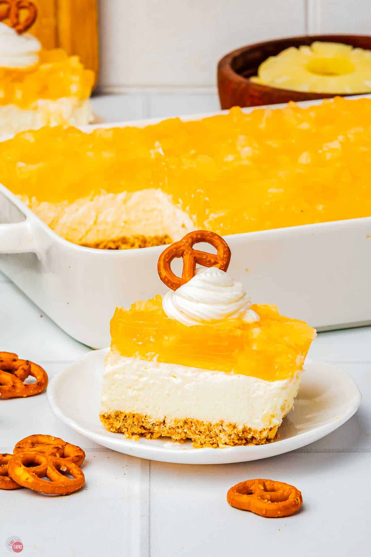 slice of pineapple pretzel salad on a plate with a casserole dish behind it