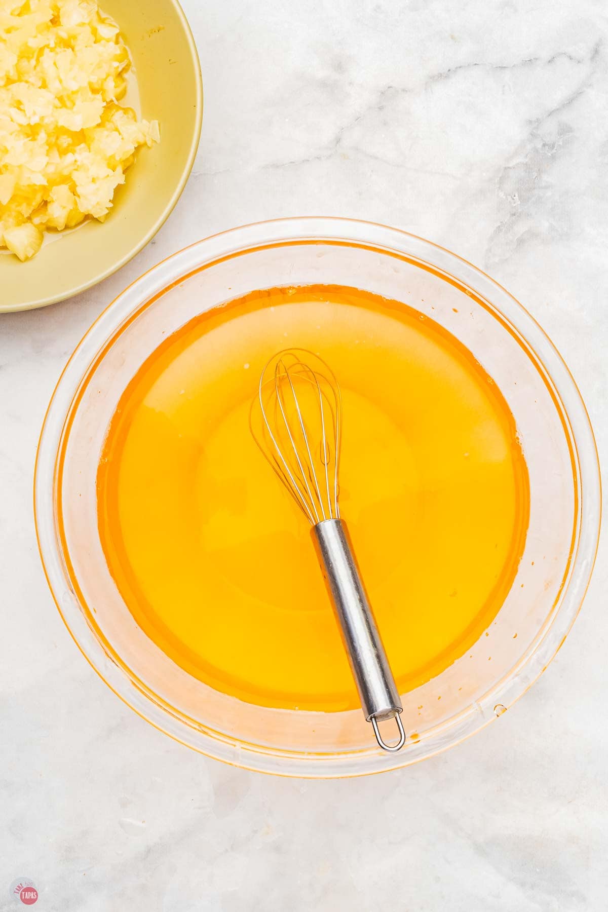 pineapple jello being stirred in a clear bowl with a whisk