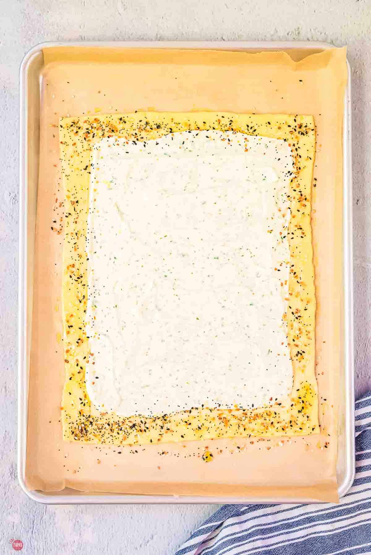 puff pastry on parchment paper with cheese and herbs spread on it