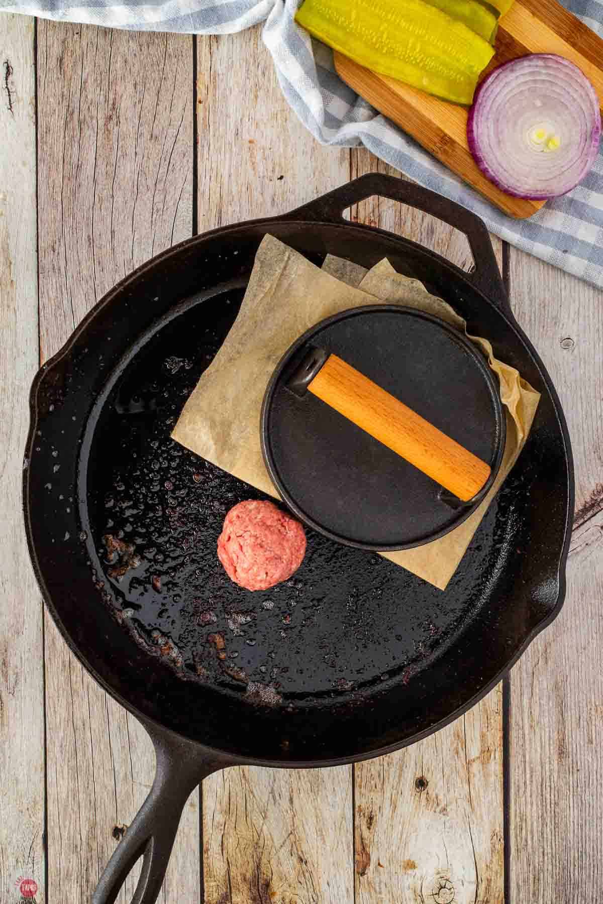 burgers cooking in a skillet with a press