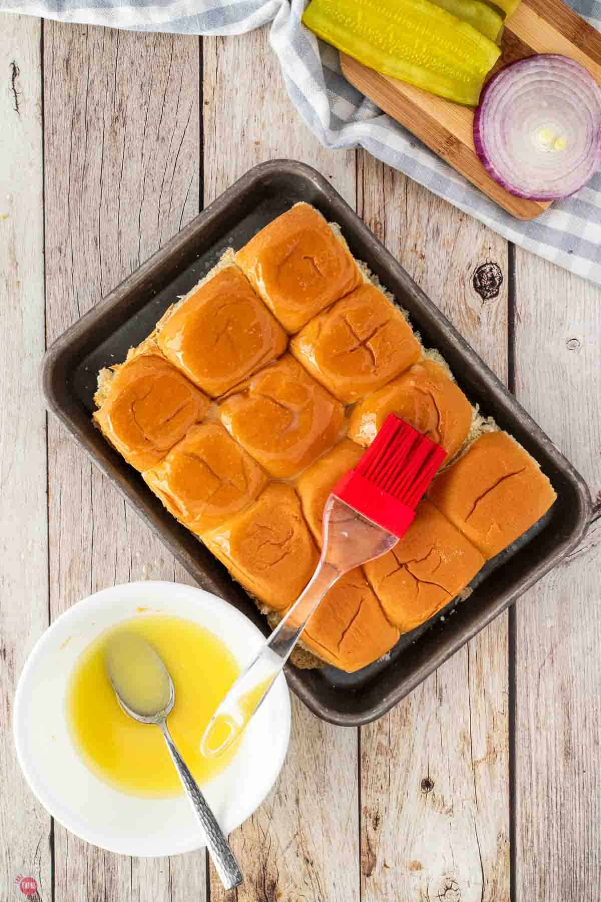 slider buns ona baking sheet being brushed with seasoned butter