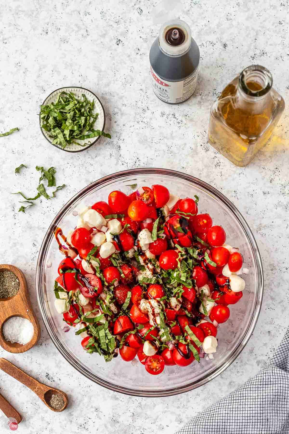 clear bowl full of grape tomatoes, mozzarella balls, and fresh basil