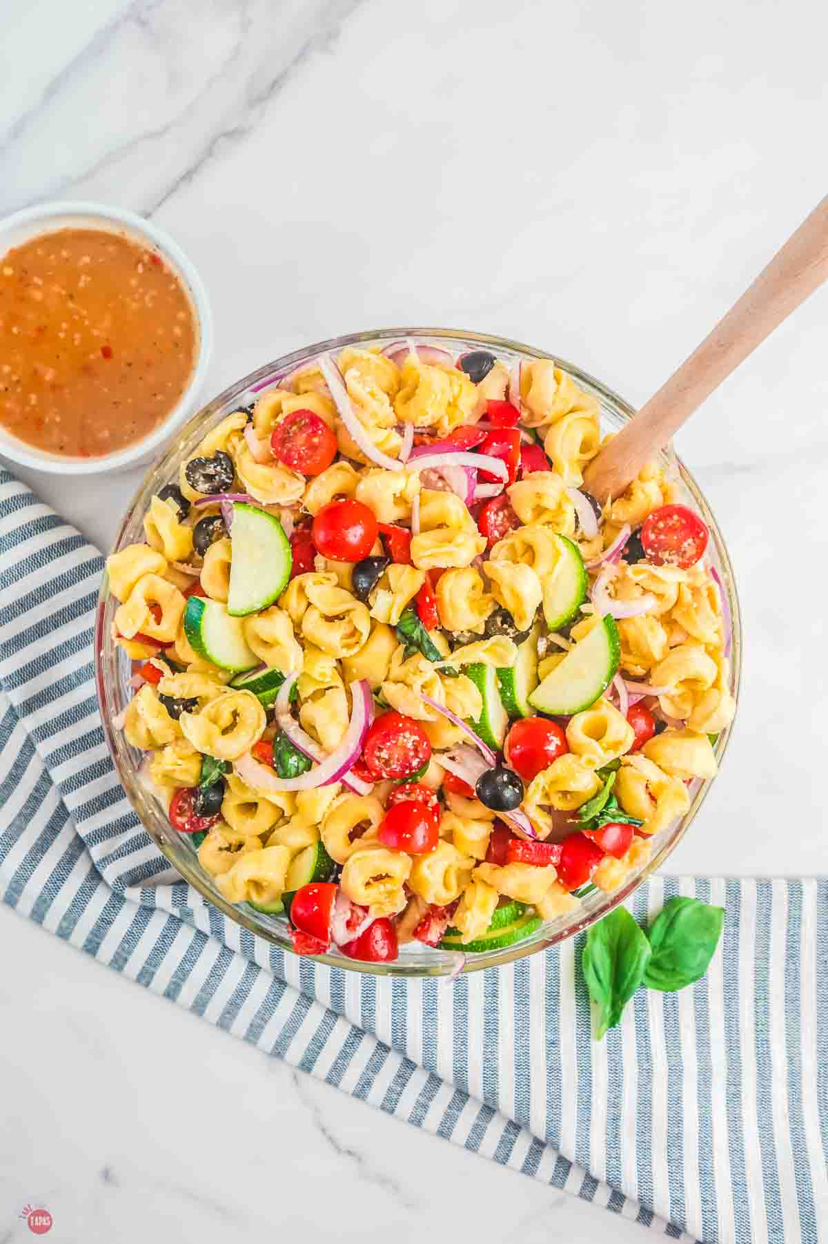 bowl of pasta salad with vegetables and a small bowl of dressing