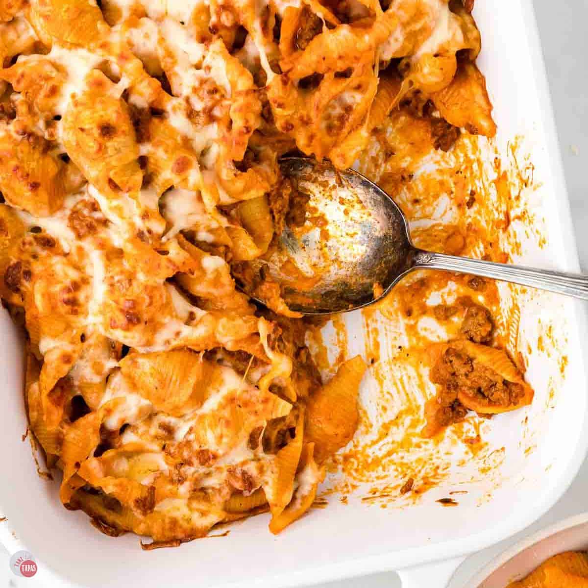 white casserole dish full of pasta and ground beef with a spoon scooping some out