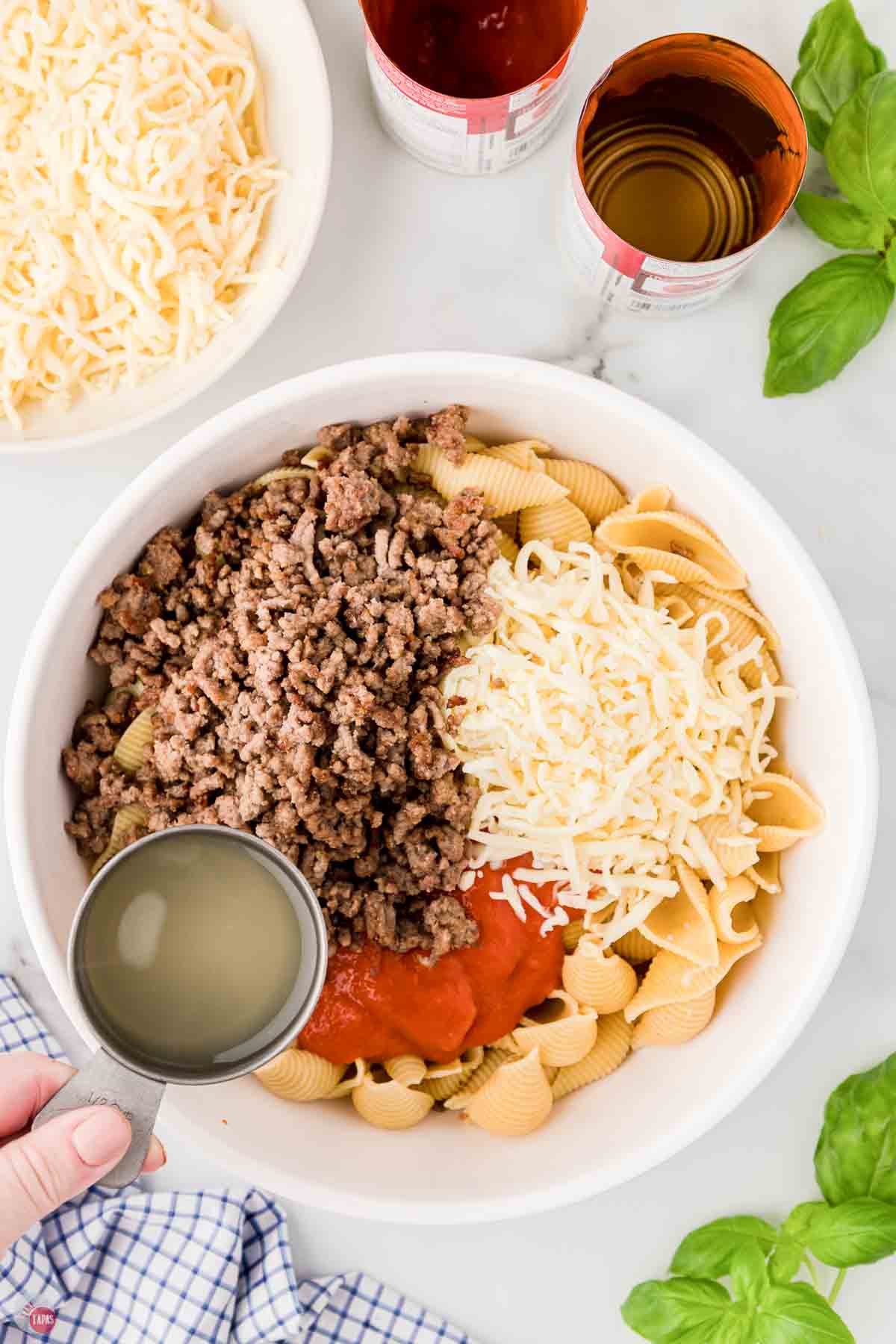 white mixing bowl with cooked noodles, ground beef, shredded cheese, and tomato soup