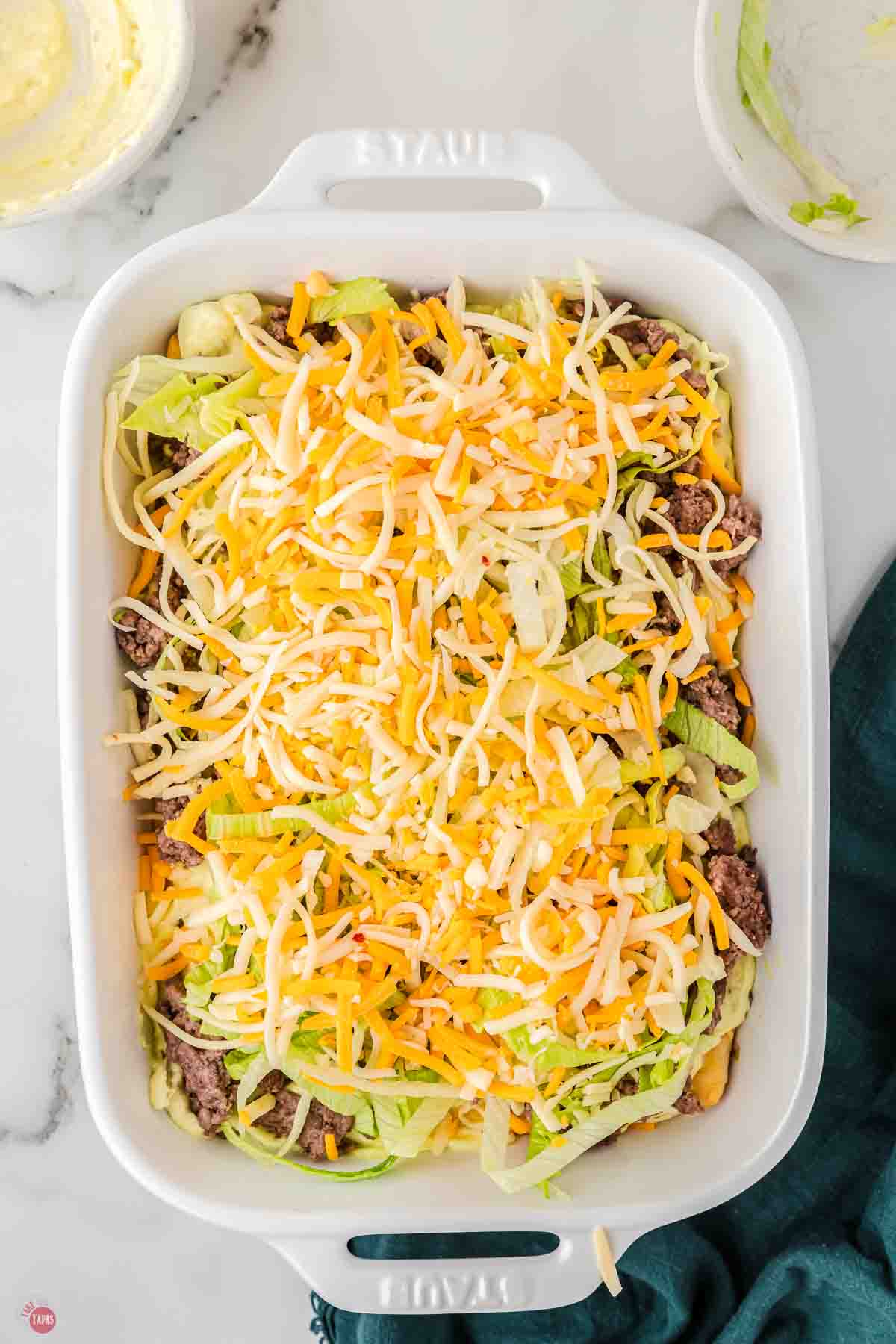 casserole dish full of ground beef, shredded lettuce, and shredded cheese