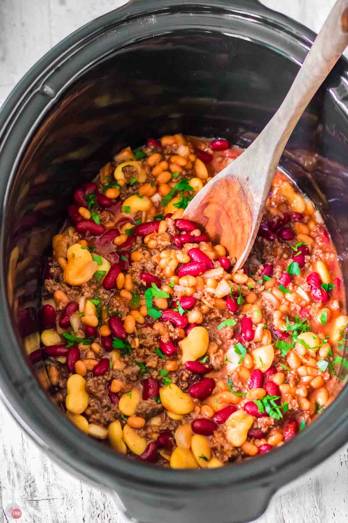 slow cooker bowl with wood spoon and ground beef and beans