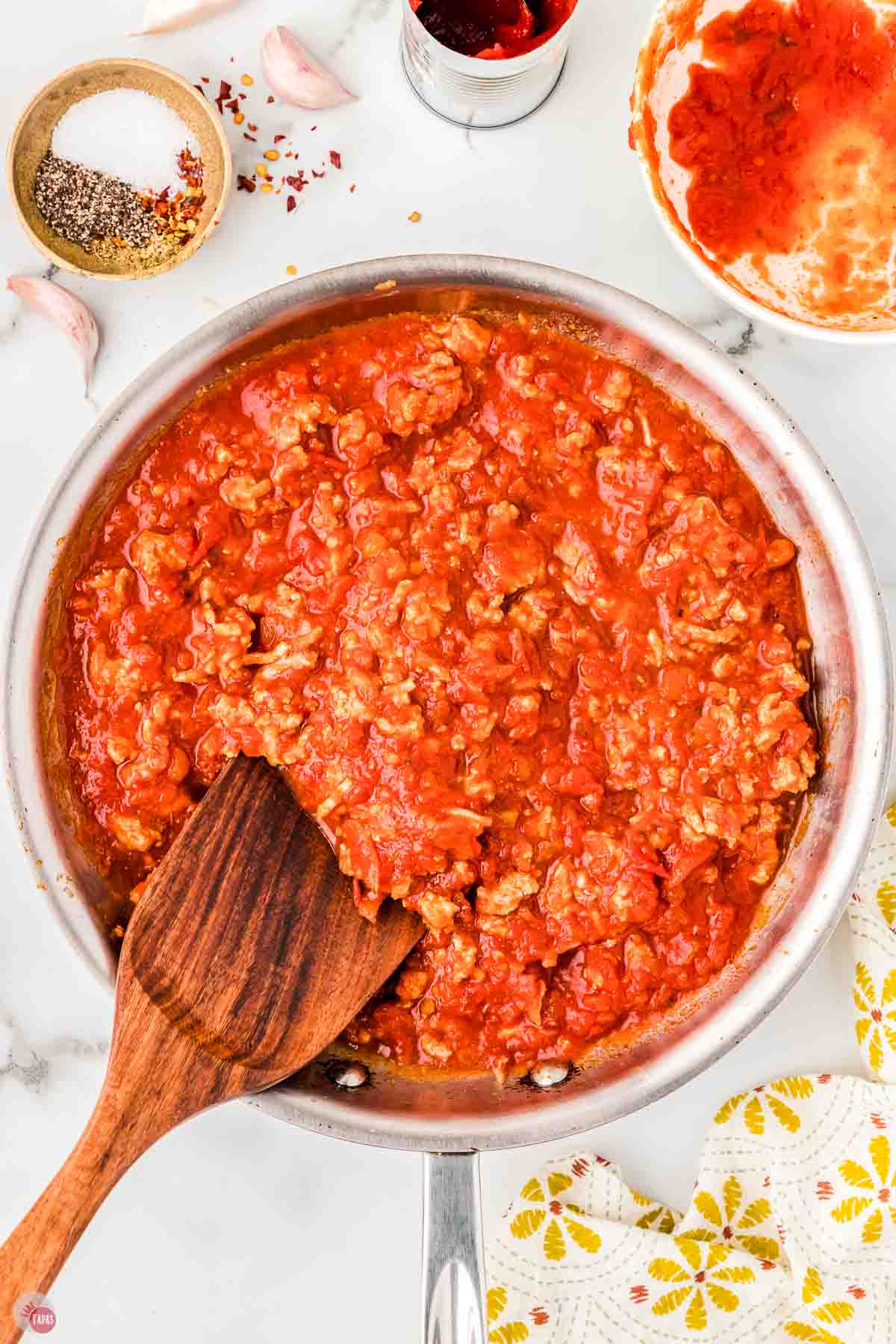 meat sauce simmering in a skillet with a wood spoon stirring it