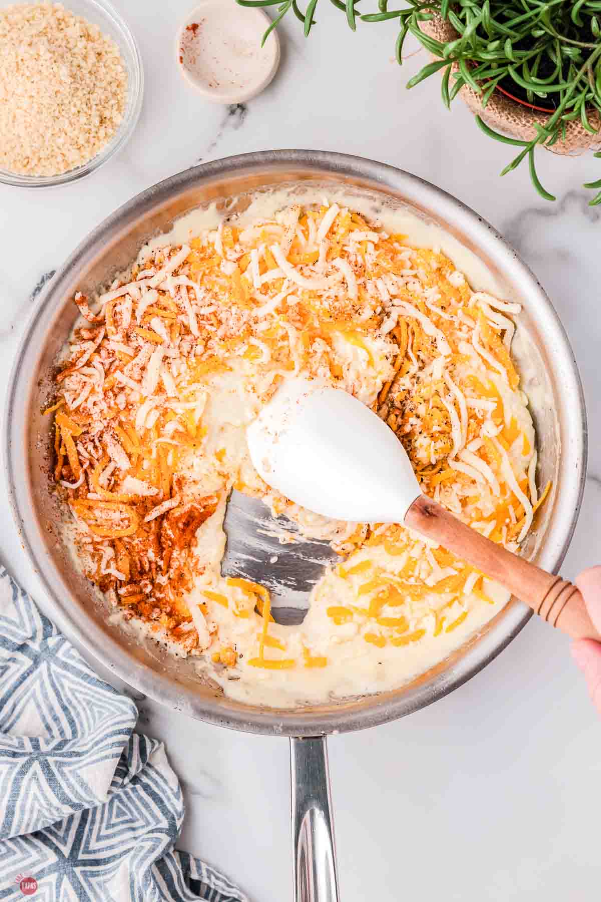 skillet with sauce and shredded cheese being stirred with a white spatula